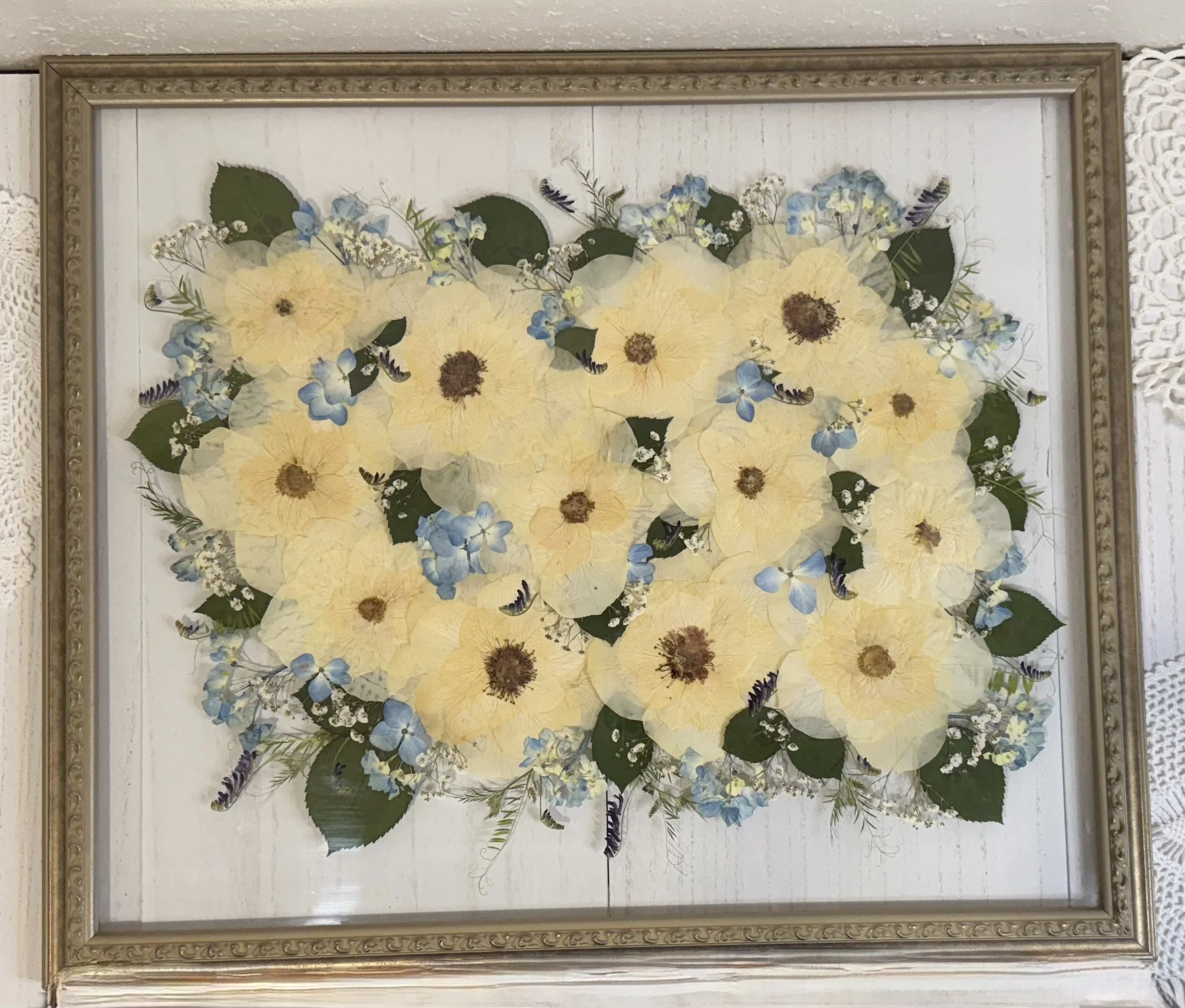 Framed flower artwork featuring yellow, white, and blue flowers and green leaves on a white background.