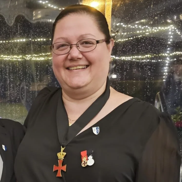 The coat of arms of the Kingdom of Hungary with a crowned shield featuring a red cross, flanked by angels, and topped with a gold crown and royal regalia. A banner at the bottom reads "non nobis dominé".