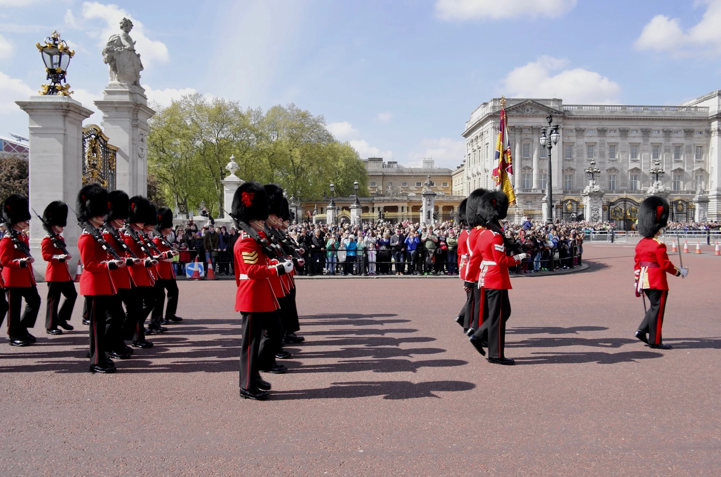 British soldiers in red uniforms and bearskin hats marching during a parade in front of Buckingham Palace in London.