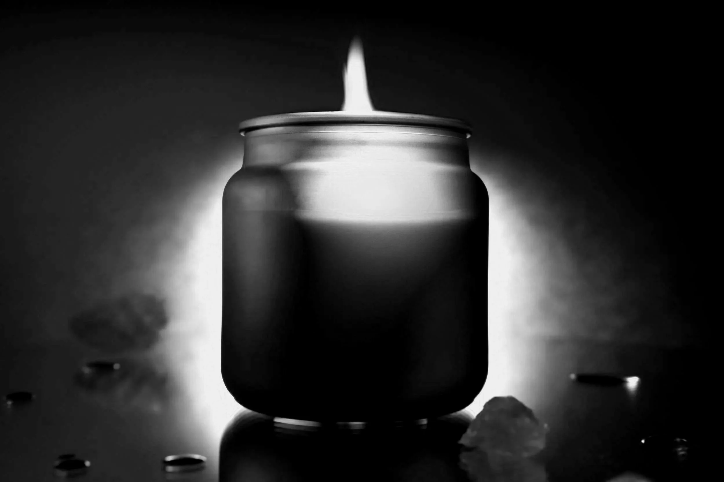 A lit candle inside a dark jar, casting a glow on the surrounding surface with scattered ice and water droplets.