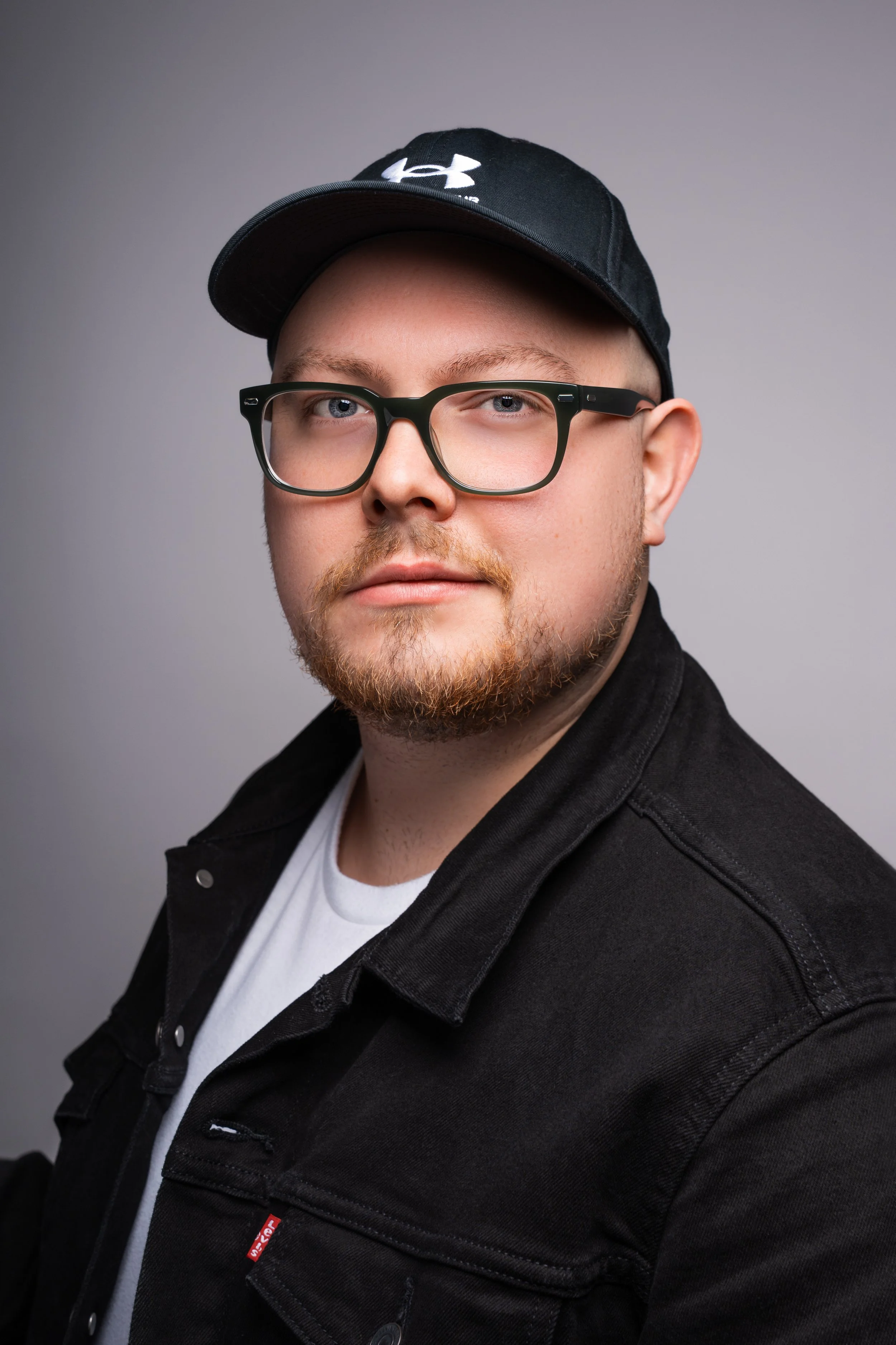 Studio portrait of a man wearing glasses and a cap against a neutral background
