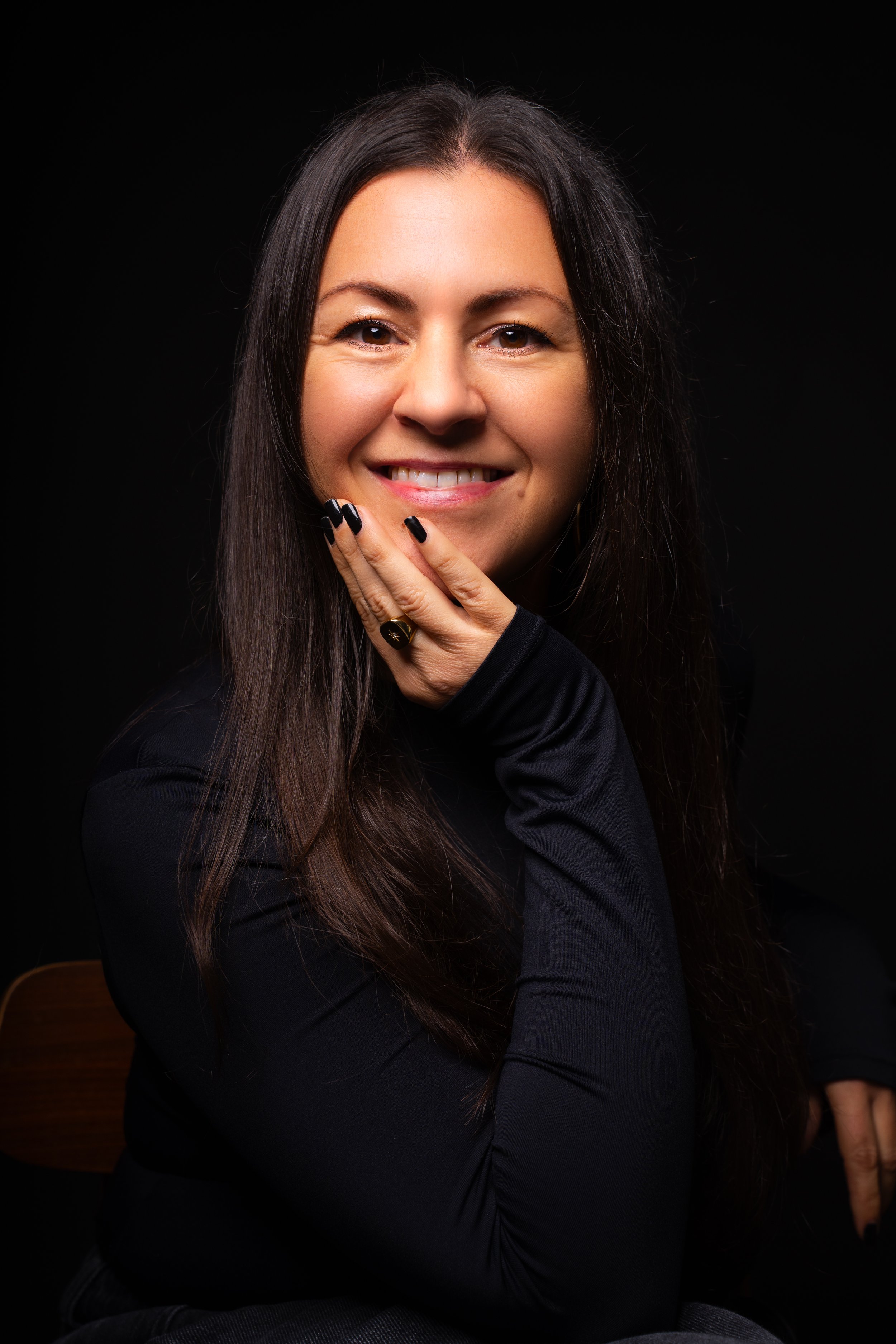 Portrait of a woman in black clothing smiling against a dark studio background