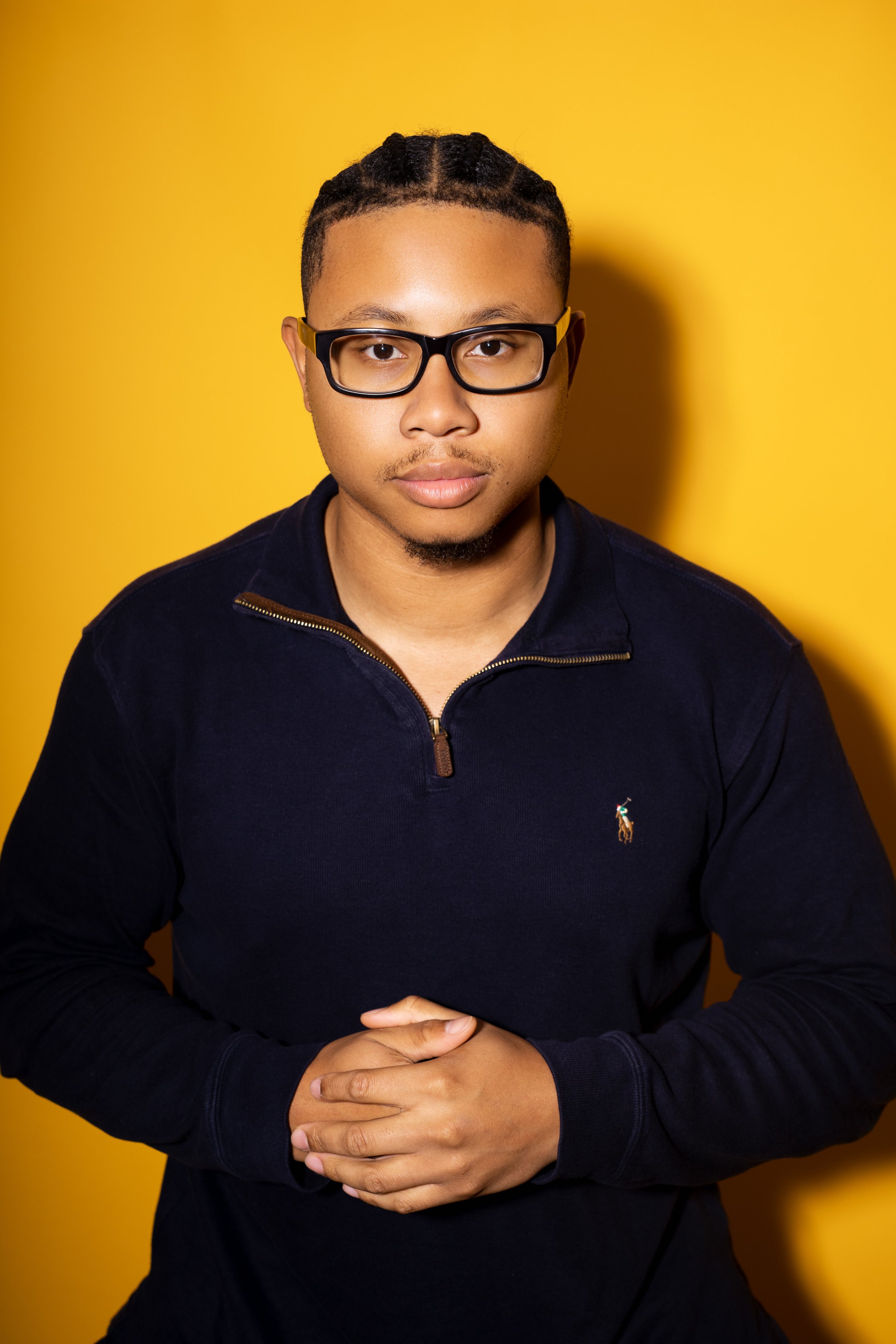 Portrait of a man with glasses against a yellow background wearing a royal blue top