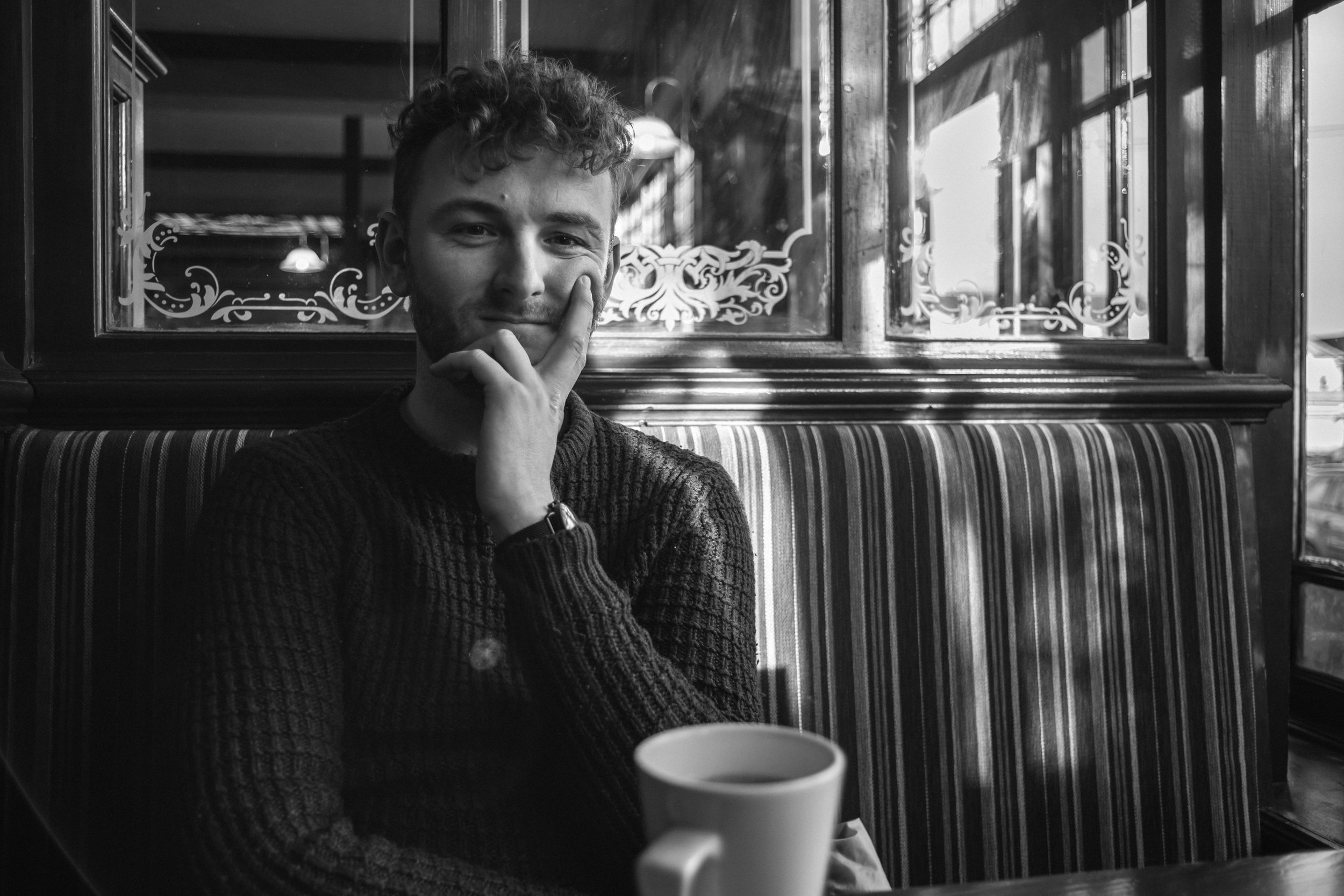 Black and white portrait of a man seated in a café next to a cup of coffee