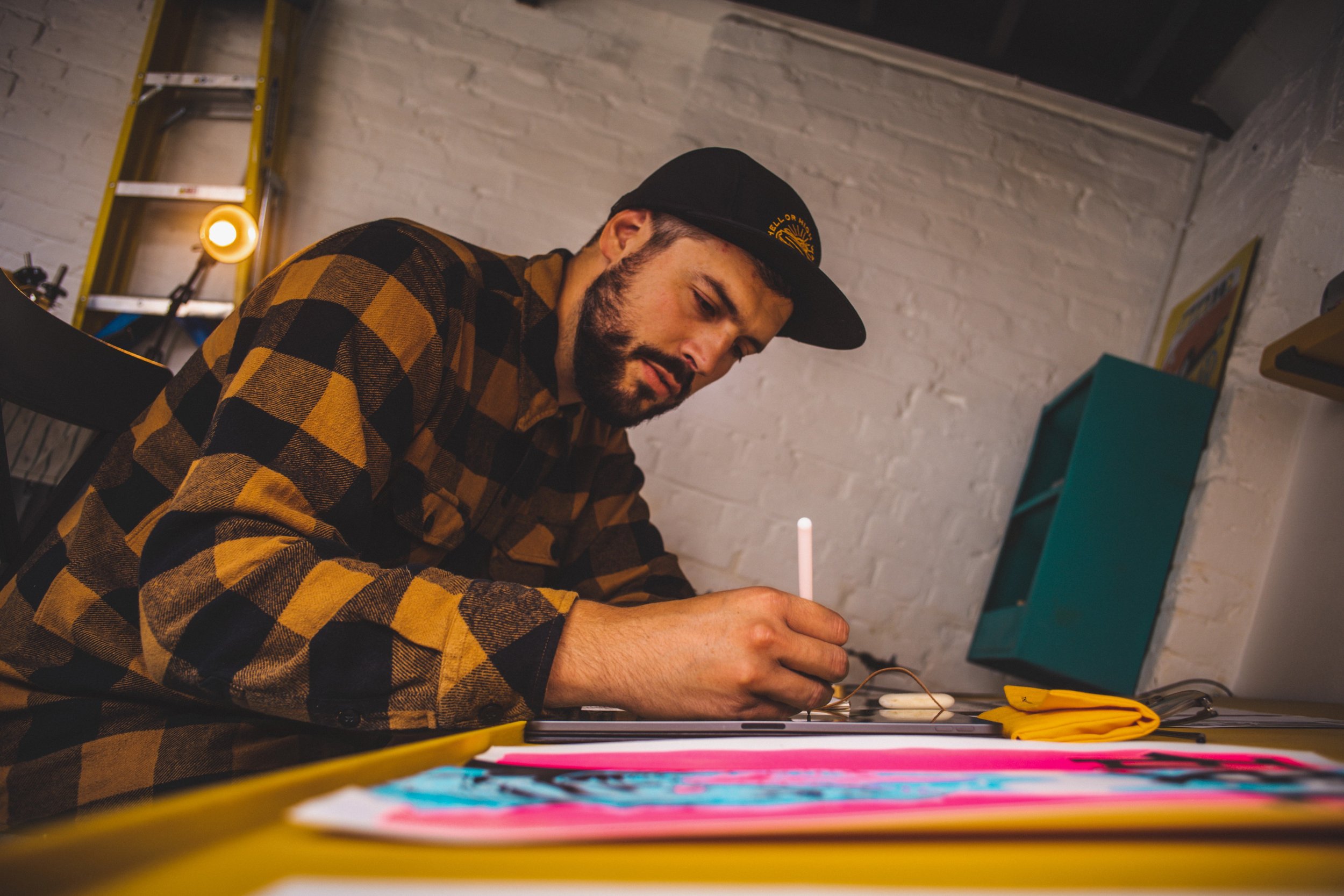 Environmental portrait of a man drawing at a desk in a studio workspace