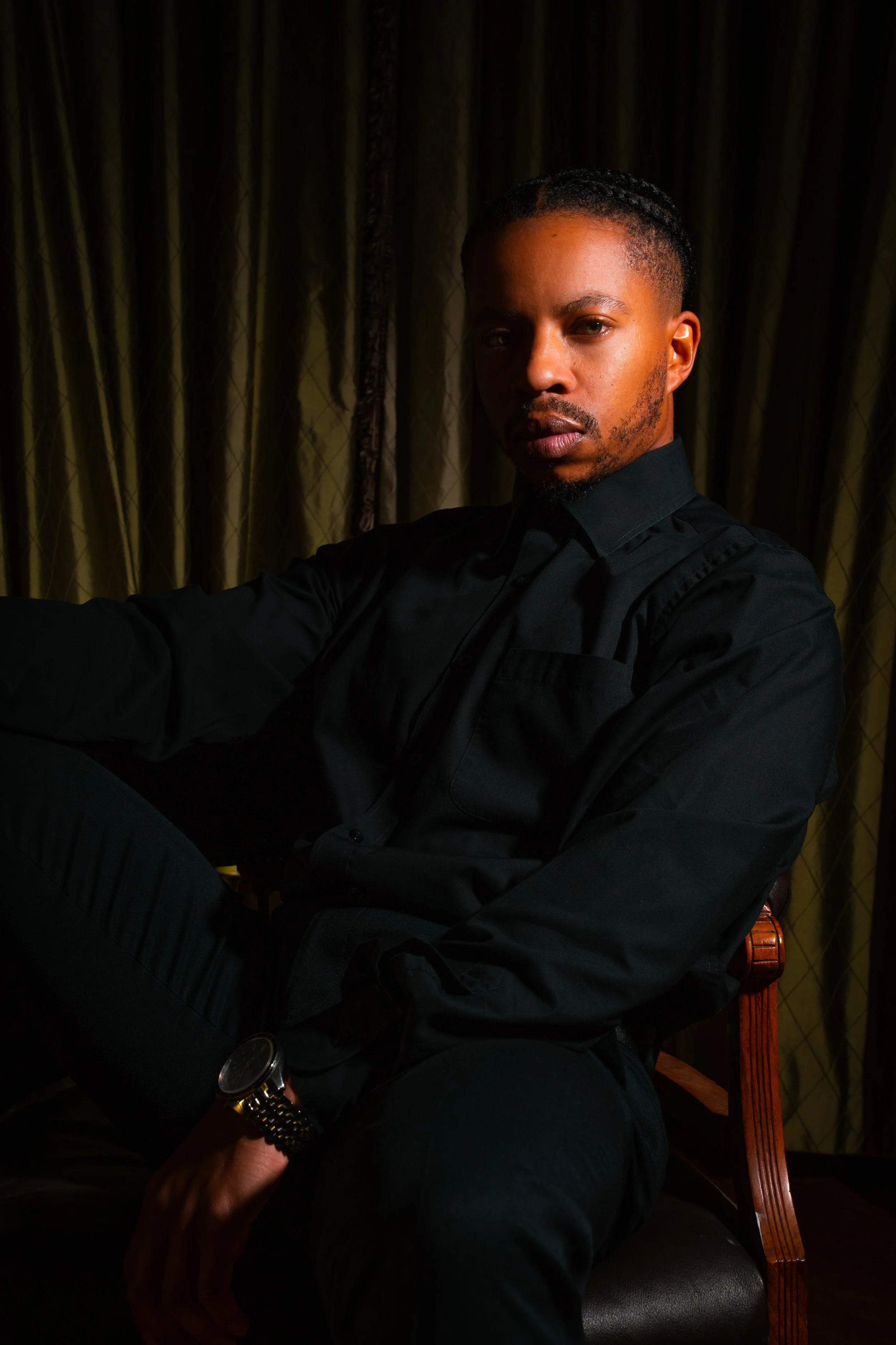 Studio portrait of a man in black clothing seated against a dark background