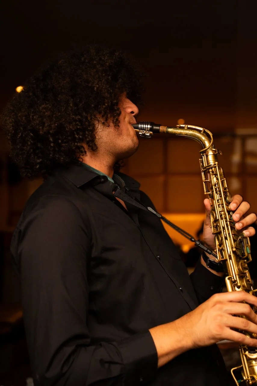A man playing a saxophone in a dimly lit indoor setting.