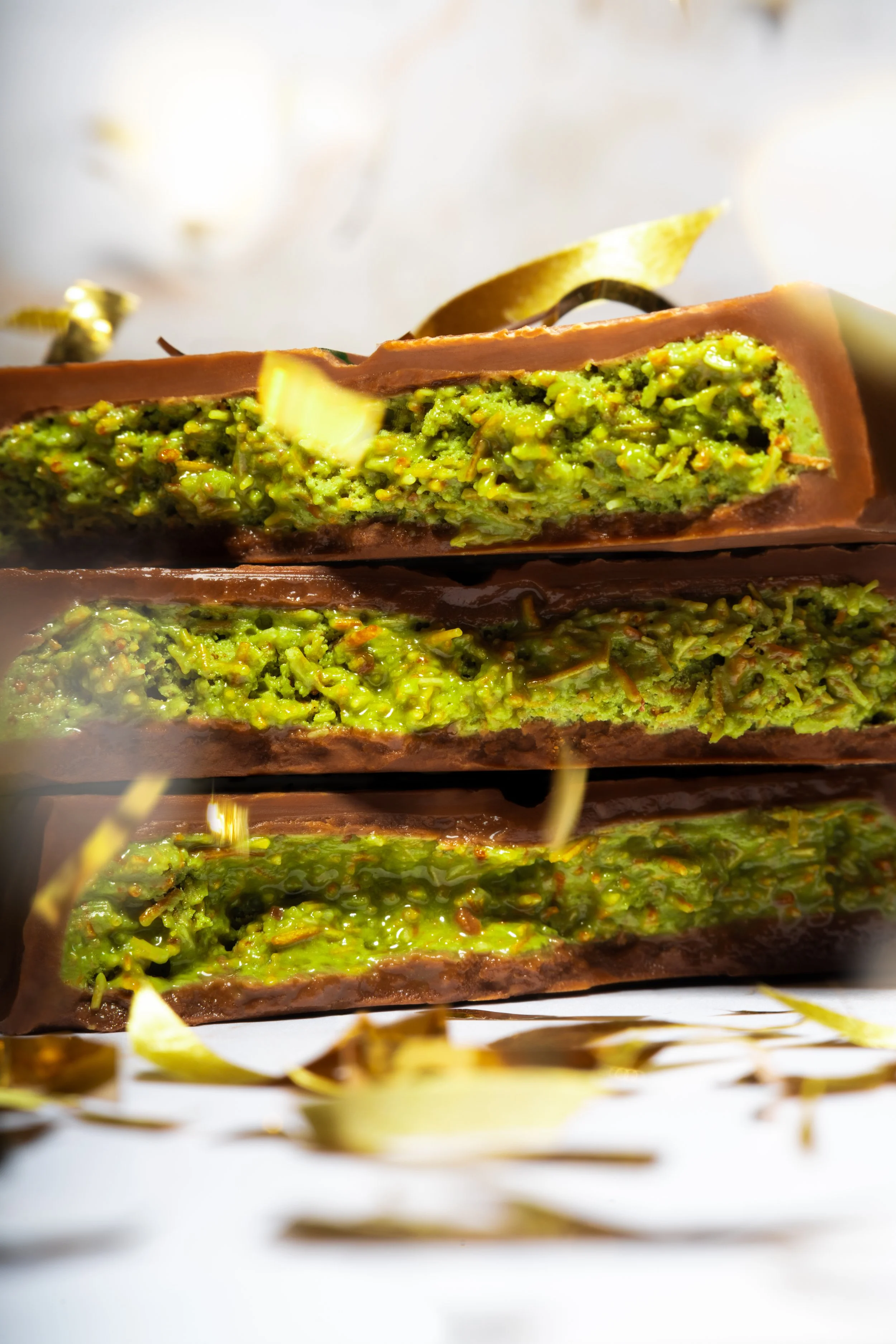 Layered pistachio-filled Dubai chocolate on a white surface, golden shavings scattered around.