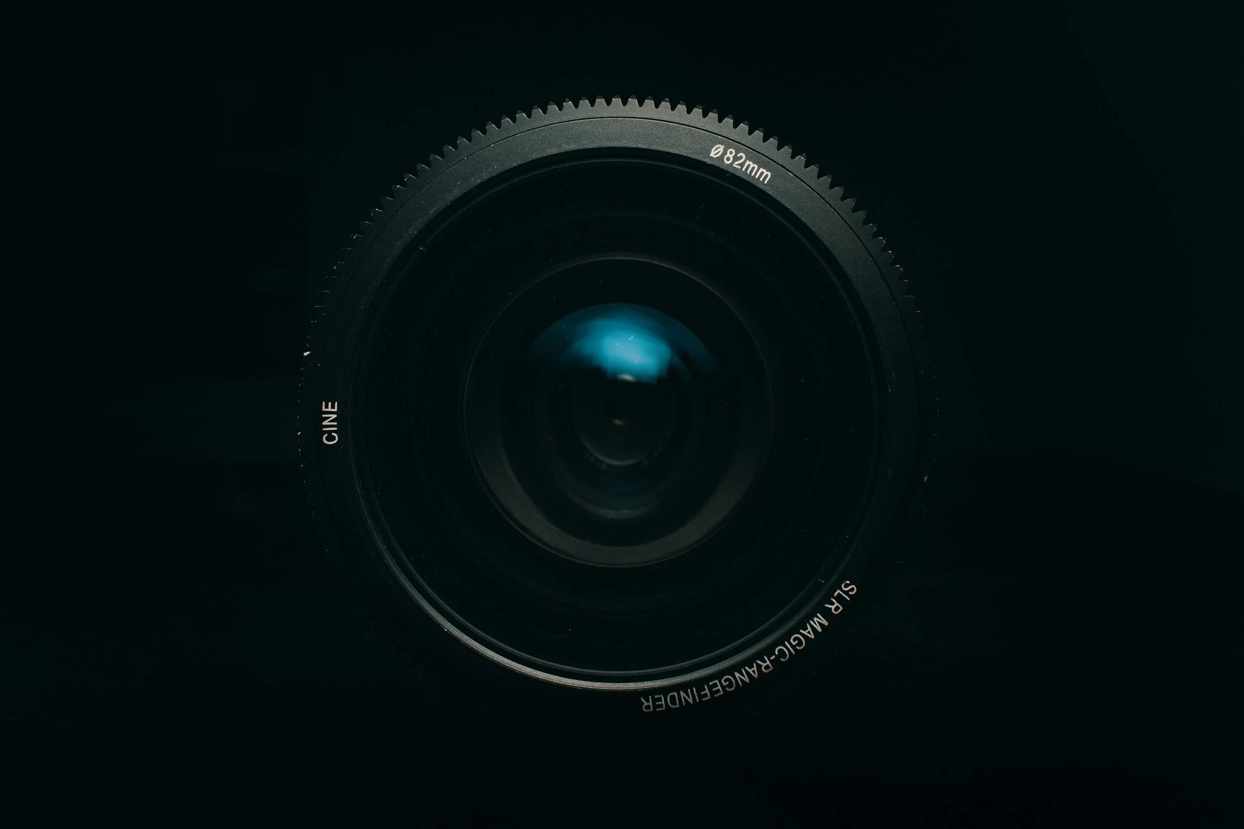 Un objectif d'appareil photo noir avec des inscriptions visibles, y compris la taille 82 mm, dans un environnement sombre.