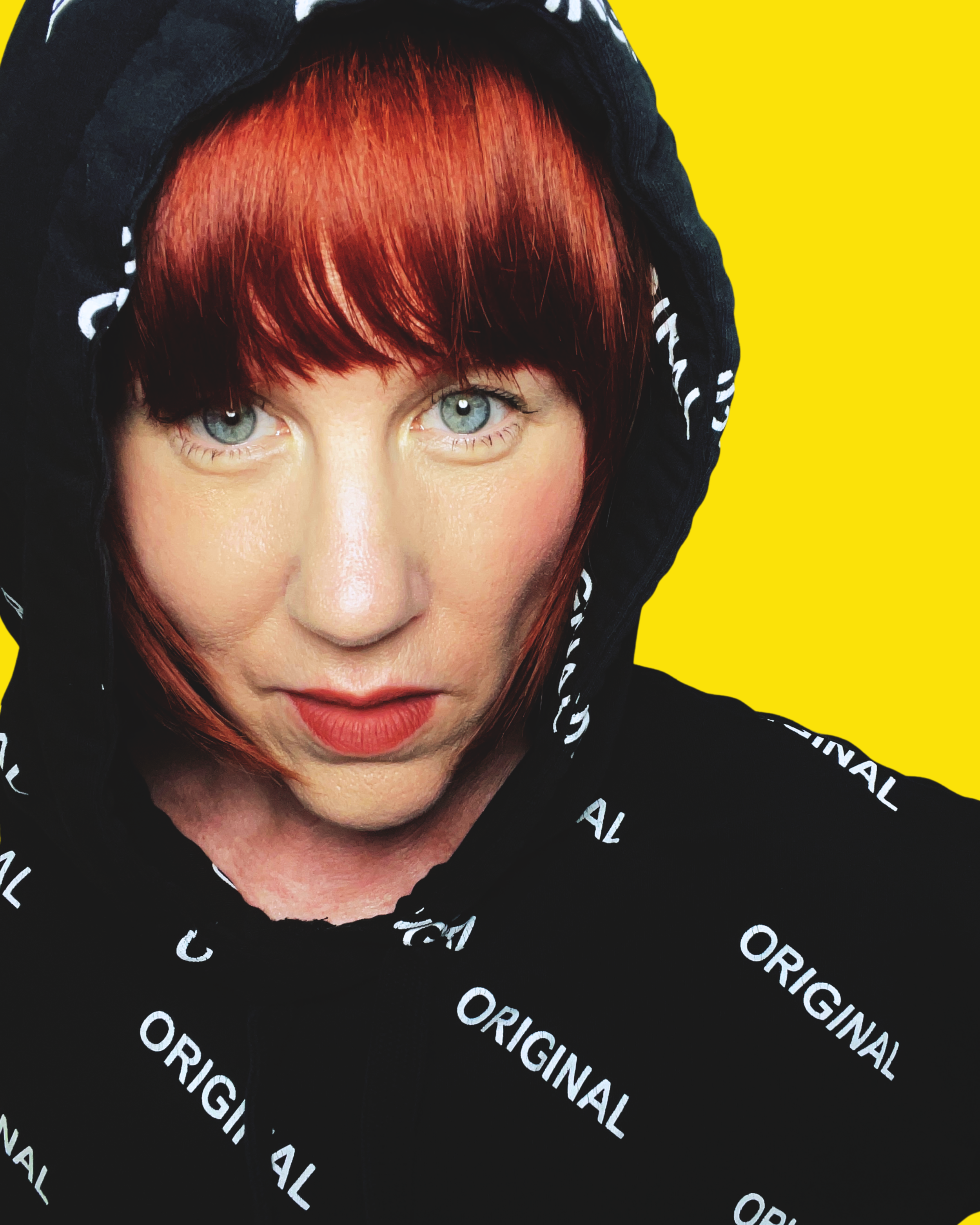 A woman with red hair and blue eyes wearing a black hoodie with white text 'ORIGINAL' on a bright yellow background.
