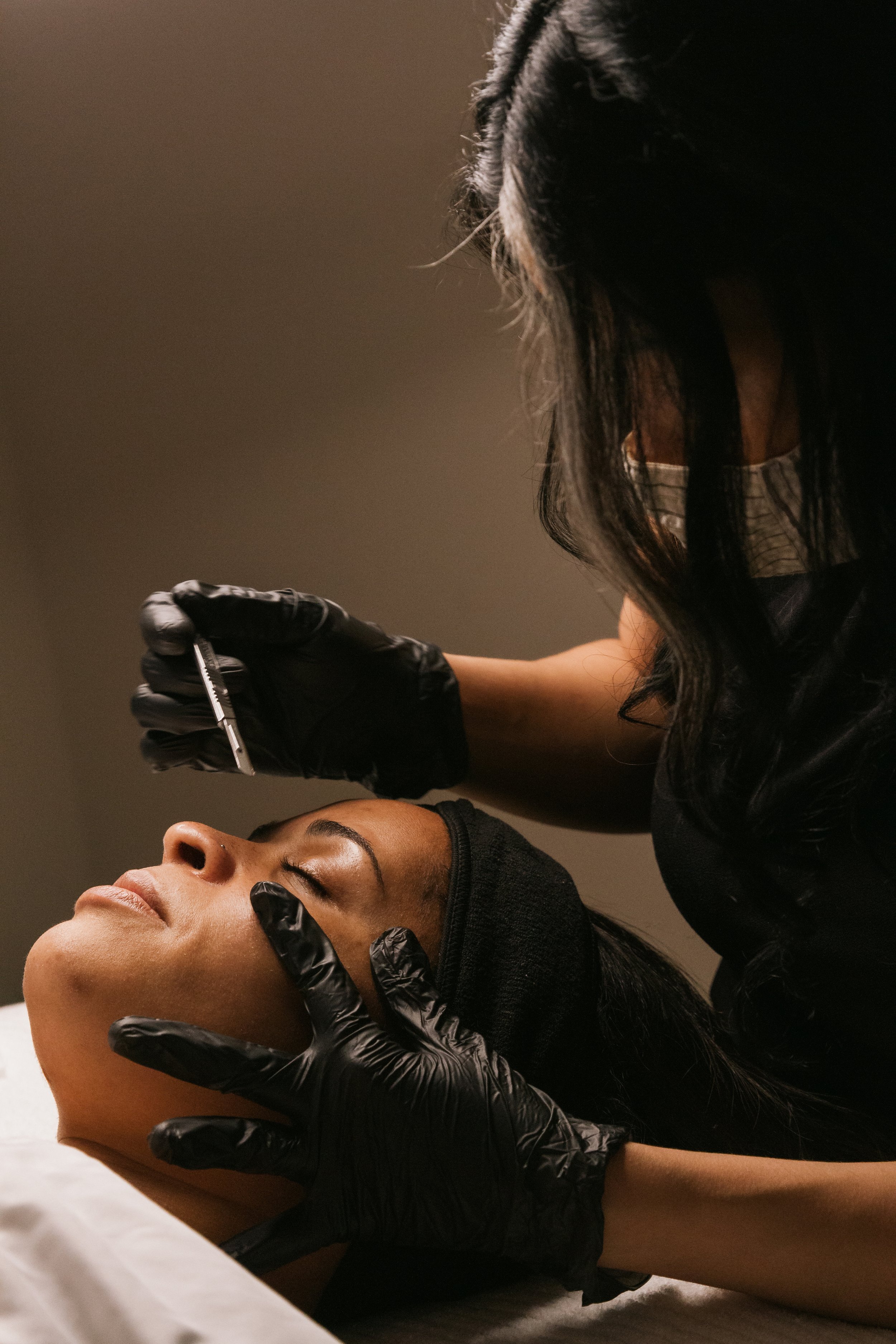 Aesthetician performing a cosmetic procedure on a woman's face.