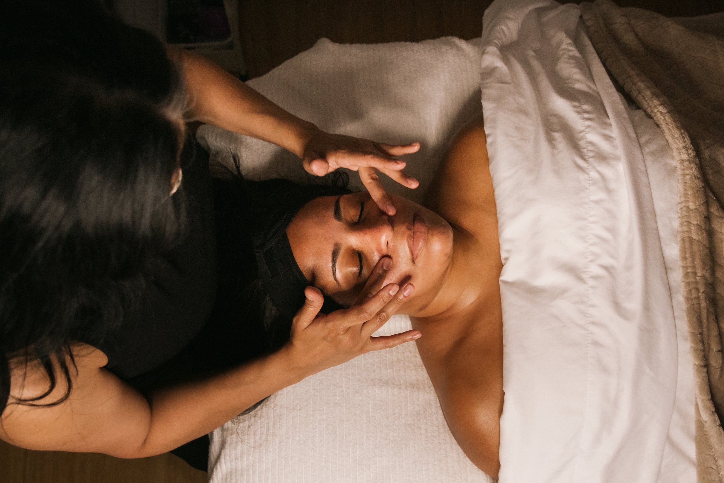 Woman receiving a face massage in a spa setting with a therapist's hands gently touching her face.