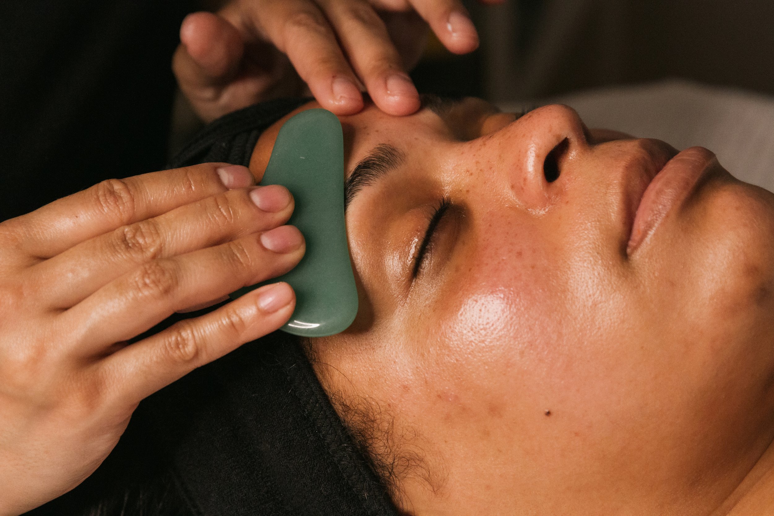 Person receiving a facial massage with a jade gua sha tool