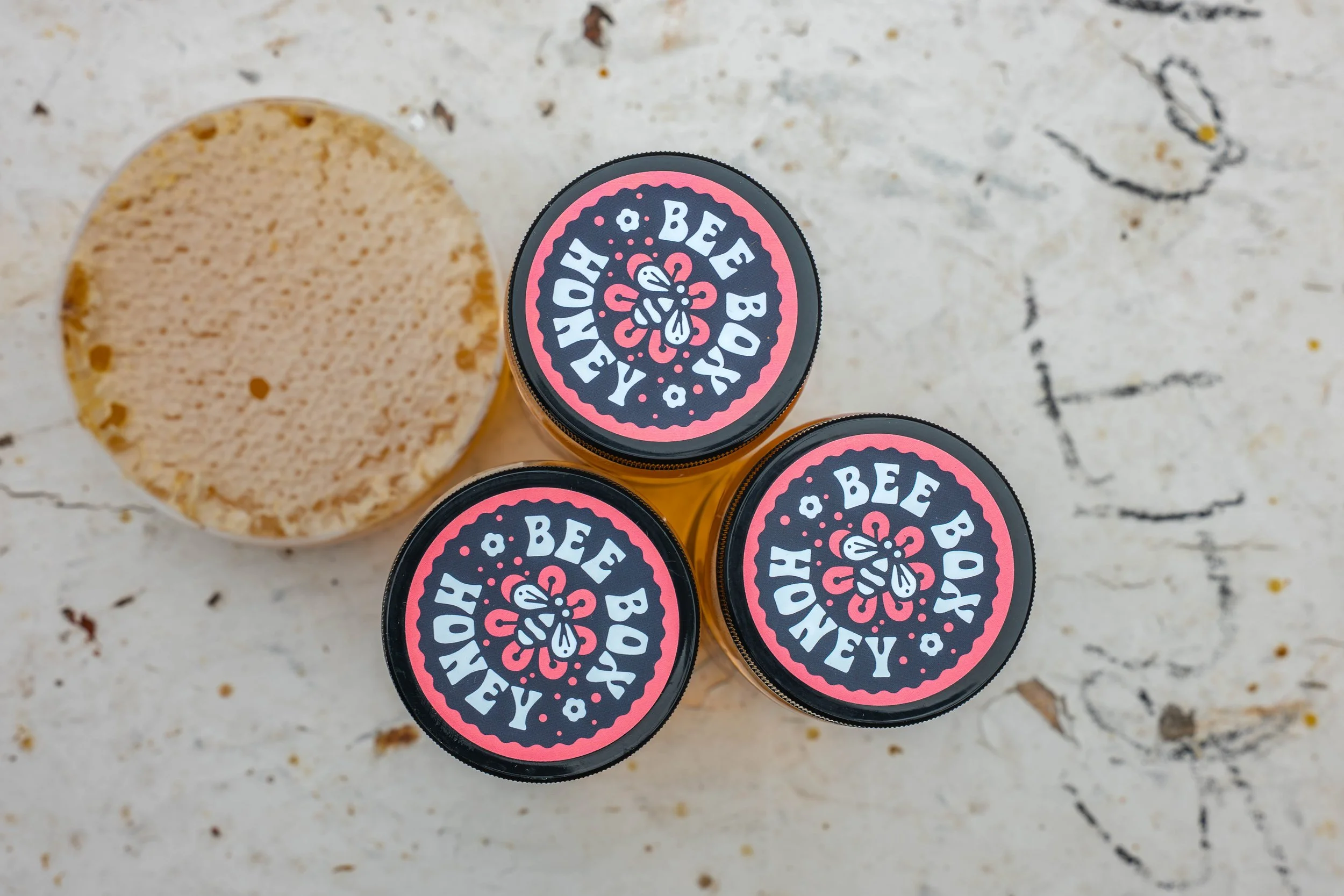 Stylized product shot of honey jars photographed against natural textures and warm golden tones.