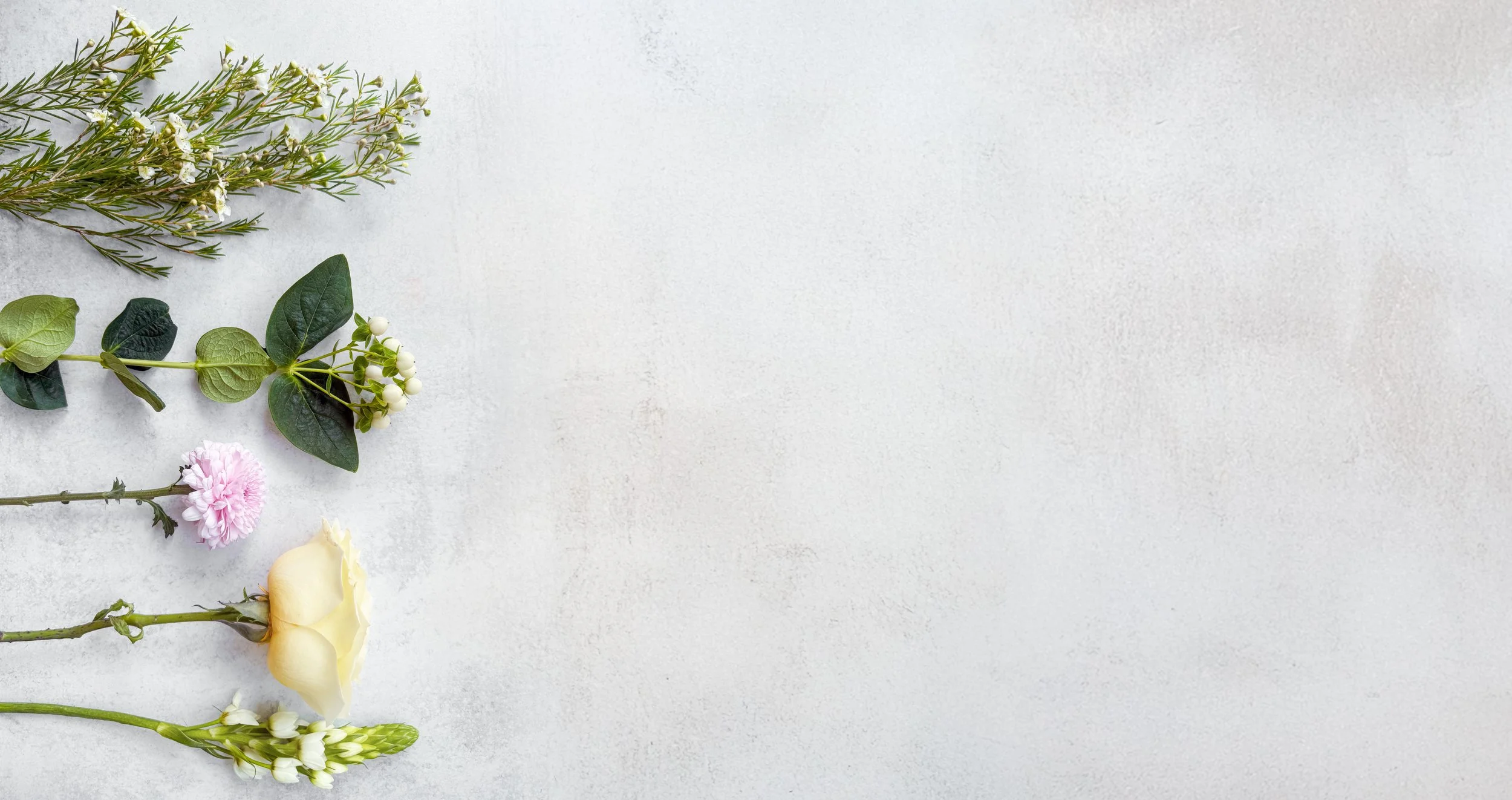 Arrangement of various flowers and greenery on a light, textured background, with space on the right.