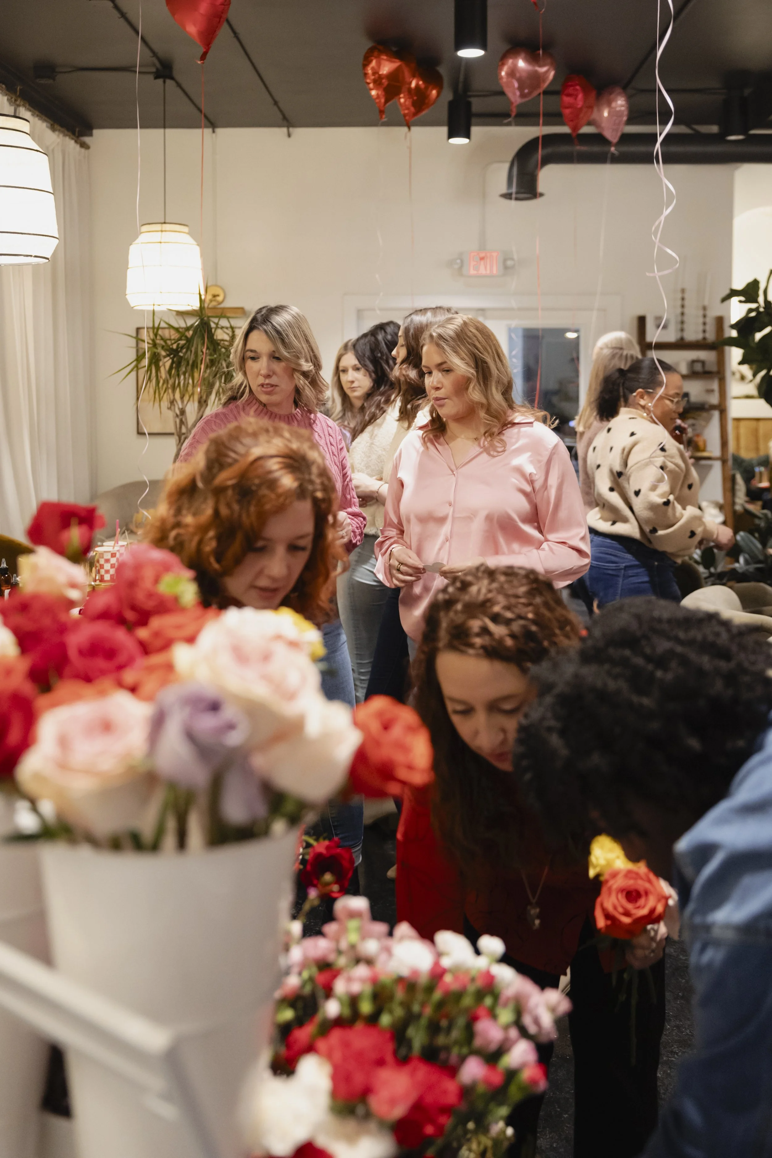 Group of women selecting flowers at a party with heart-shaped balloons hanging from the ceiling.