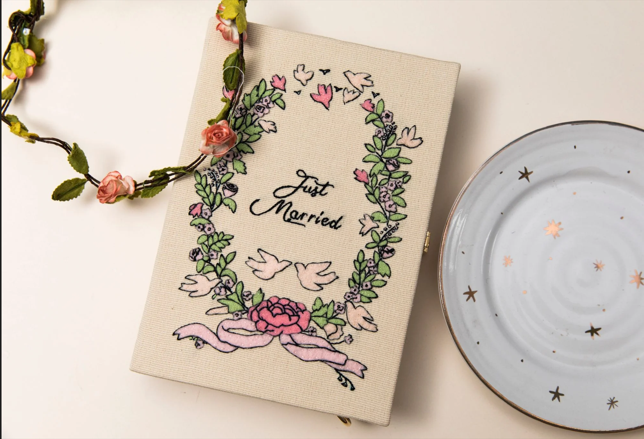 Livre de mariage avec décoration florale, une guirlande de fleurs roses en haut à gauche, une assiette blanche avec des étoiles dorées à droite.