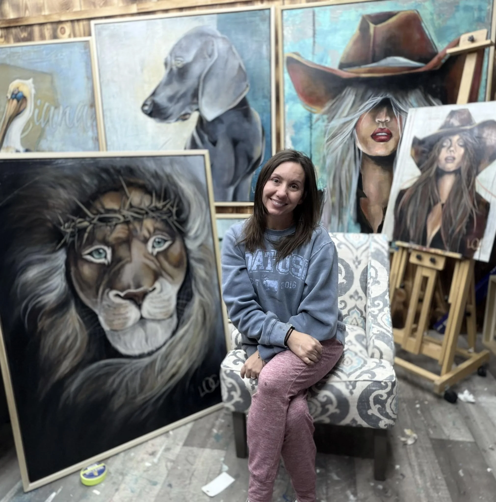 An artist creating a realism painting of a woman wearing a large, wide-brimmed hat, with her face partially hidden by her hair, with other paintings in progress around her.