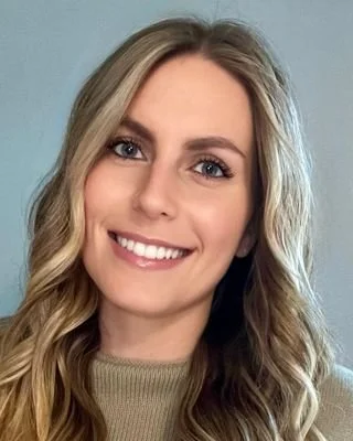 A smiling woman with long blonde hair and blue eyes, wearing a beige top.