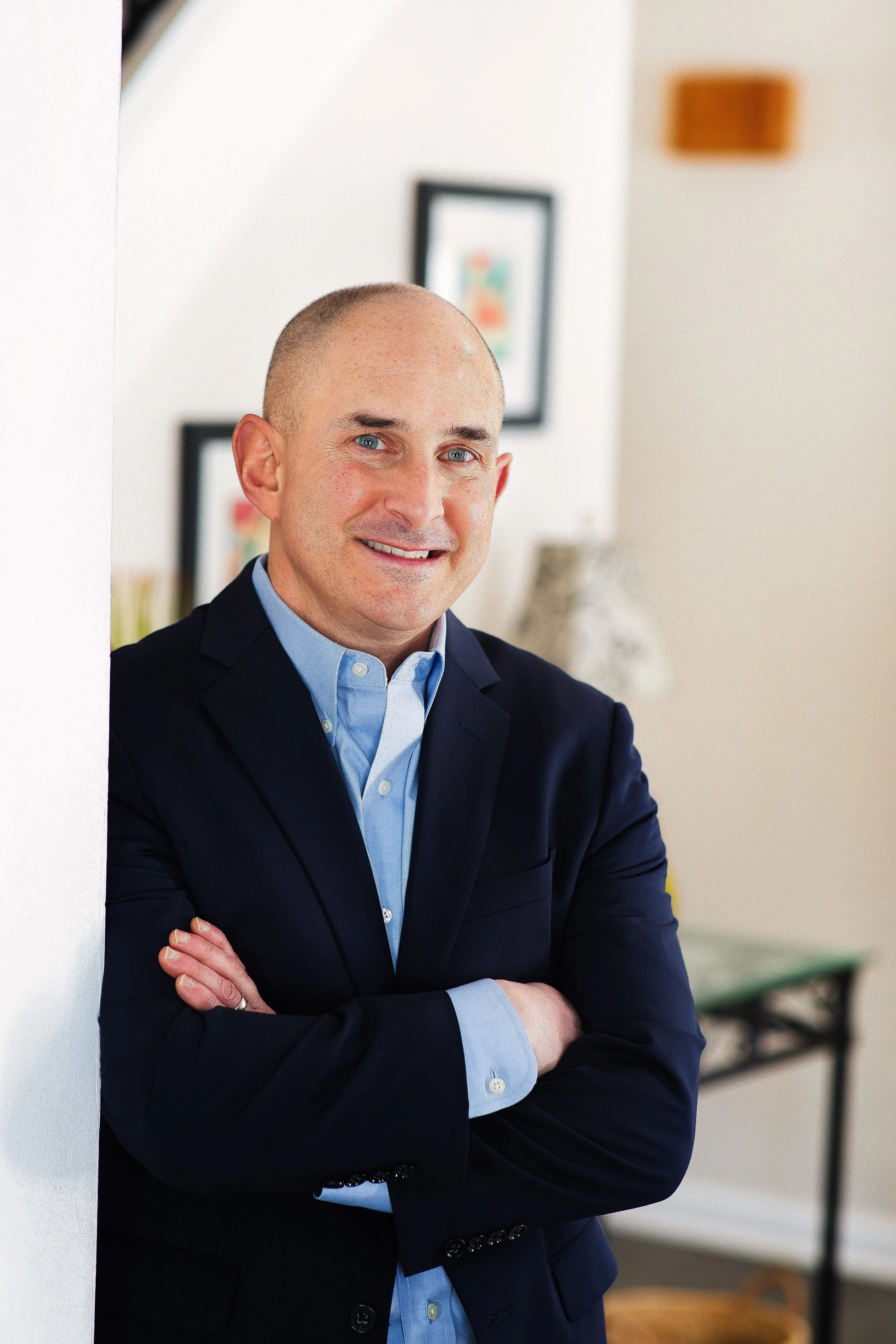Professional branding headshot of man in blazer with arms crossed, smiling indoors