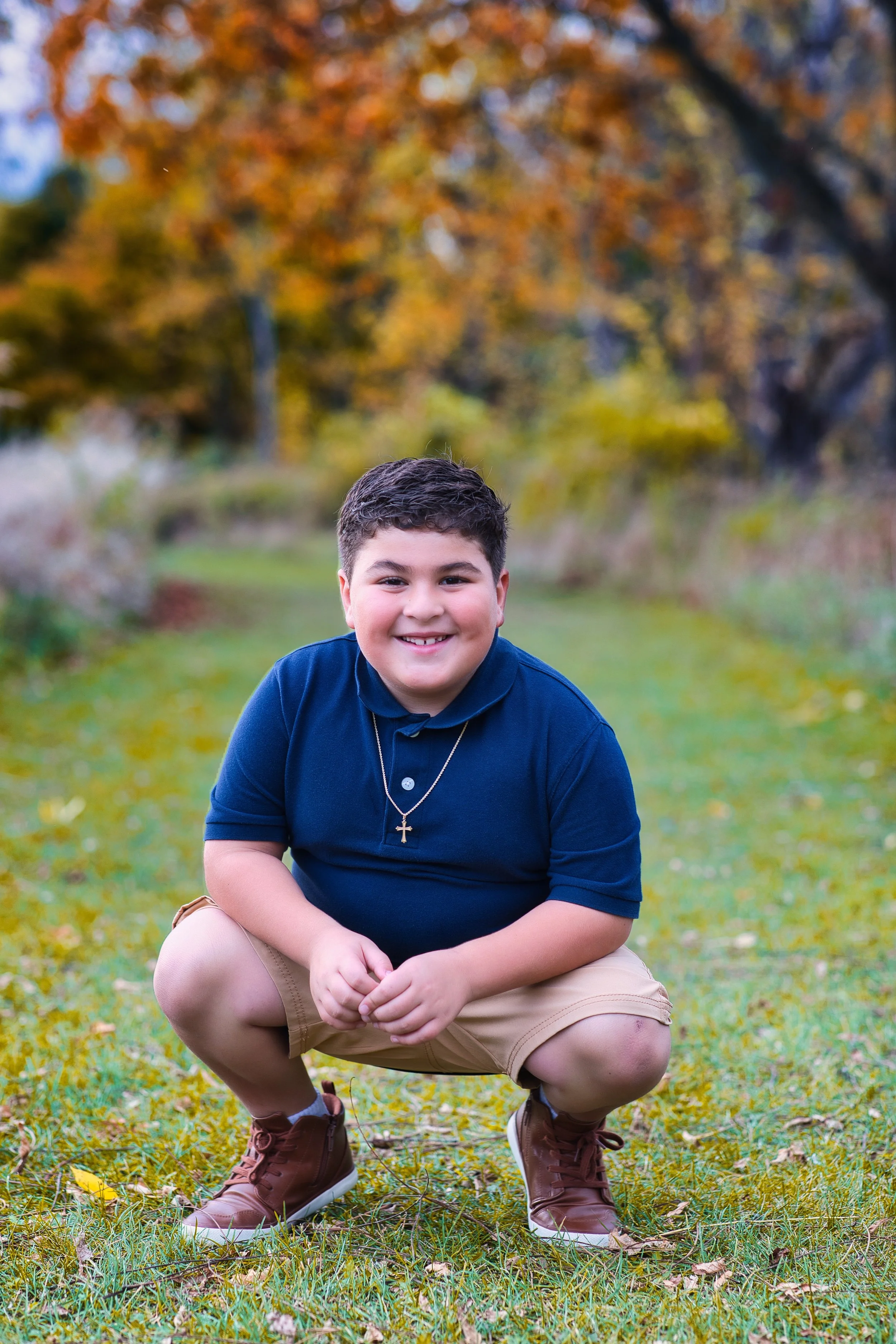 Rochester, NY portrait of a young boy crouching and smiling outdoors in fall