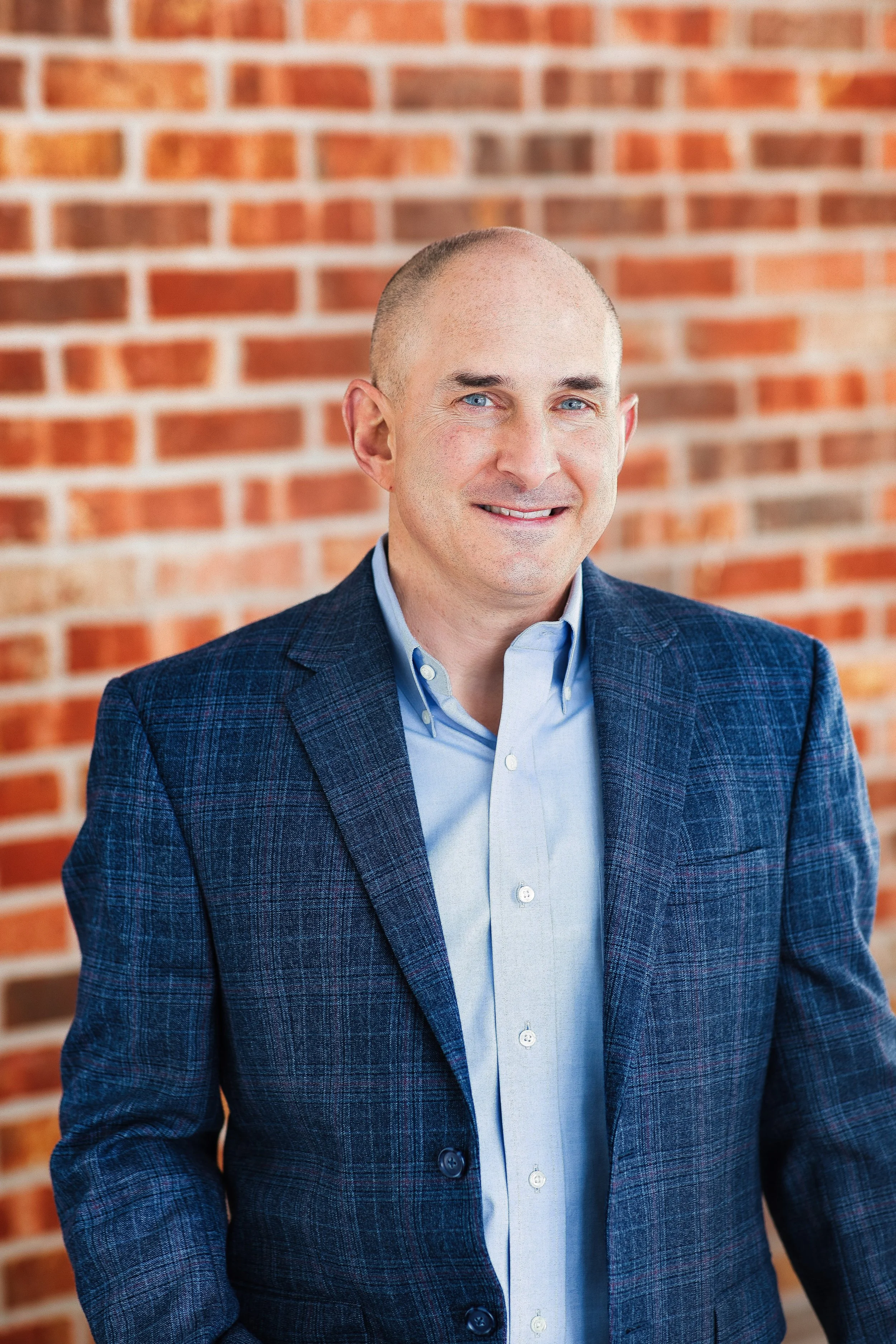 Branding headshot of man in textured blazer in front of brick wall, confident expression