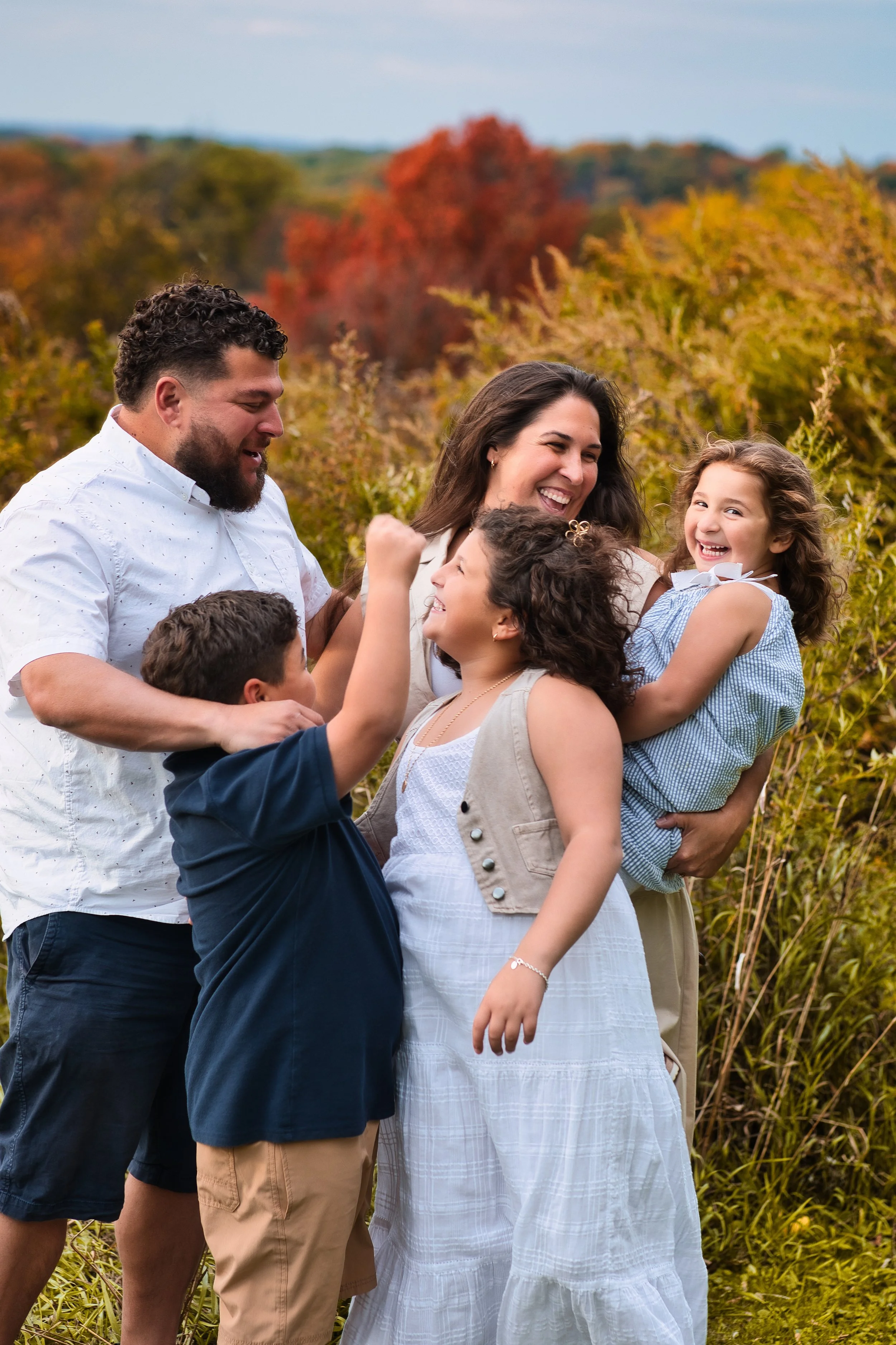 Rochester, NY family portrait of parents playing with children in a fall field