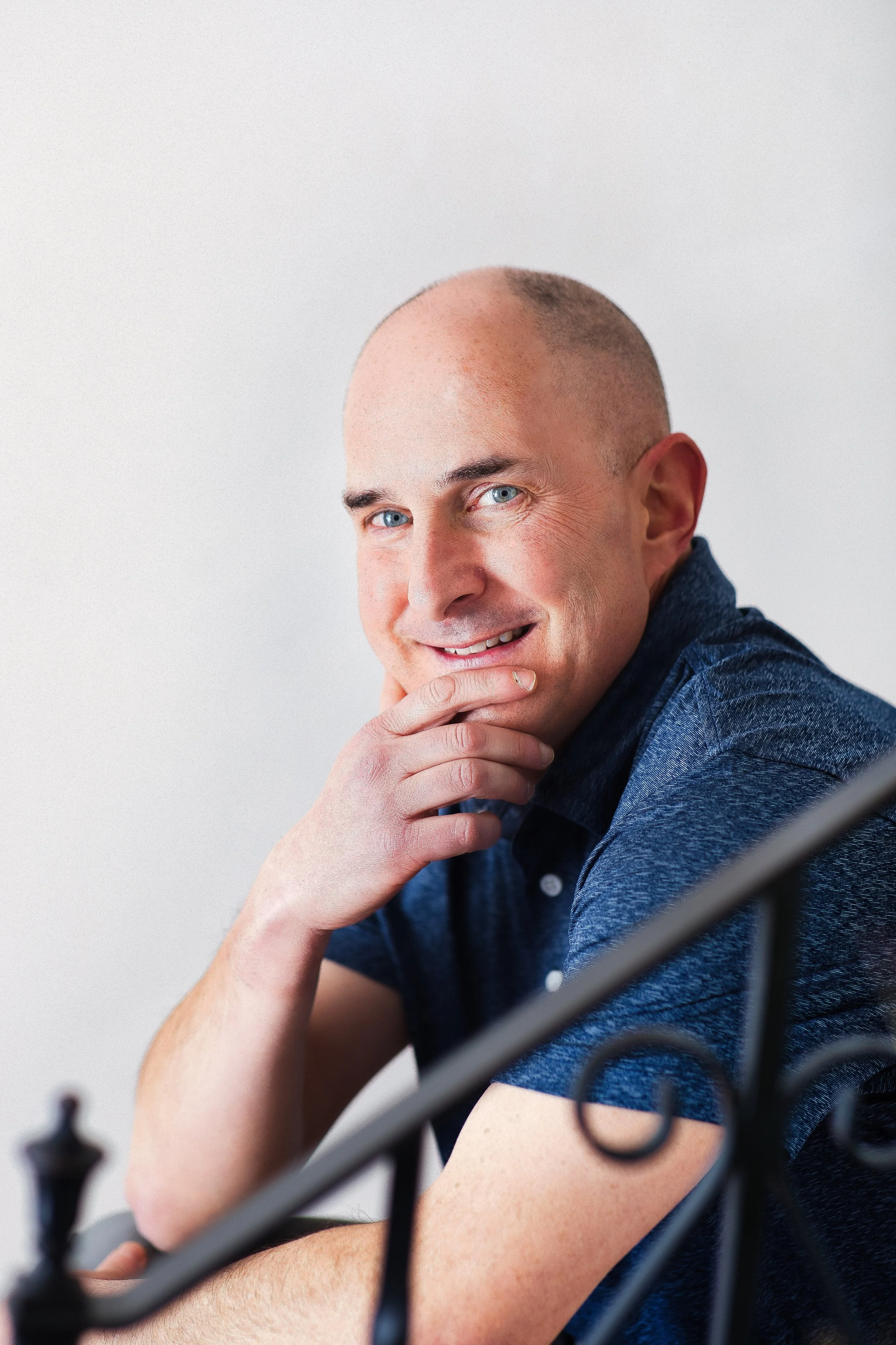 Corporate headshot of man leaning on railing with hand on chin, thoughtful expression