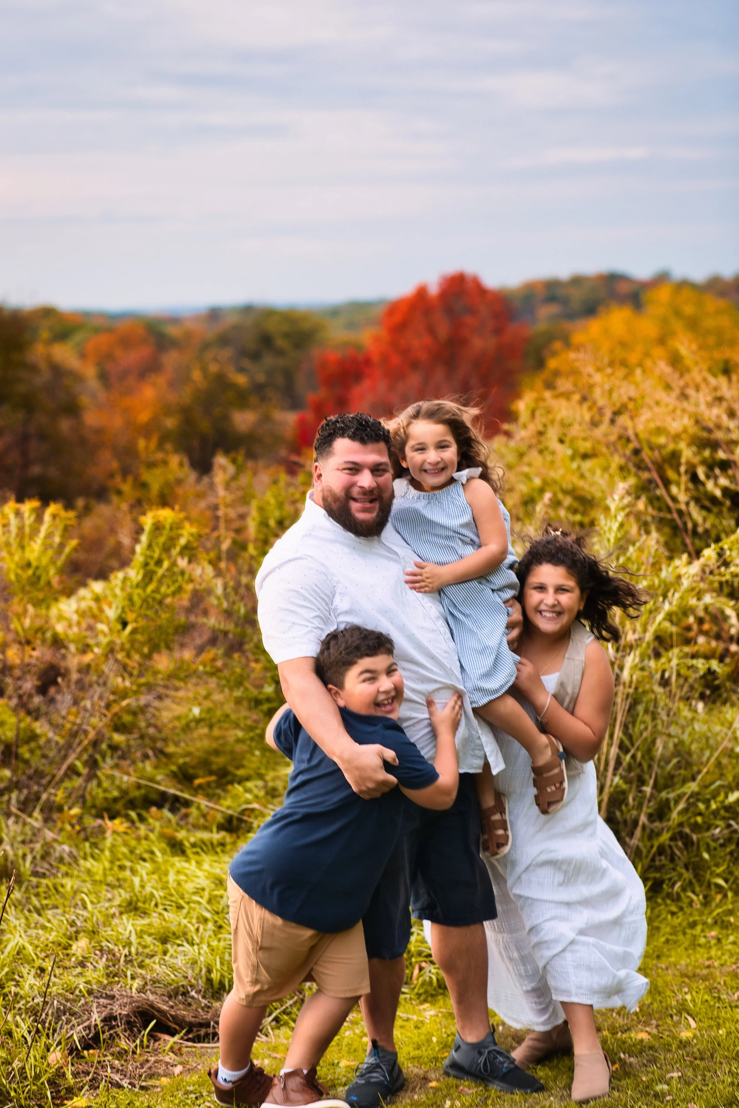 Rochester, NY family portrait of father holding and hugging children with colorful fall foliage background