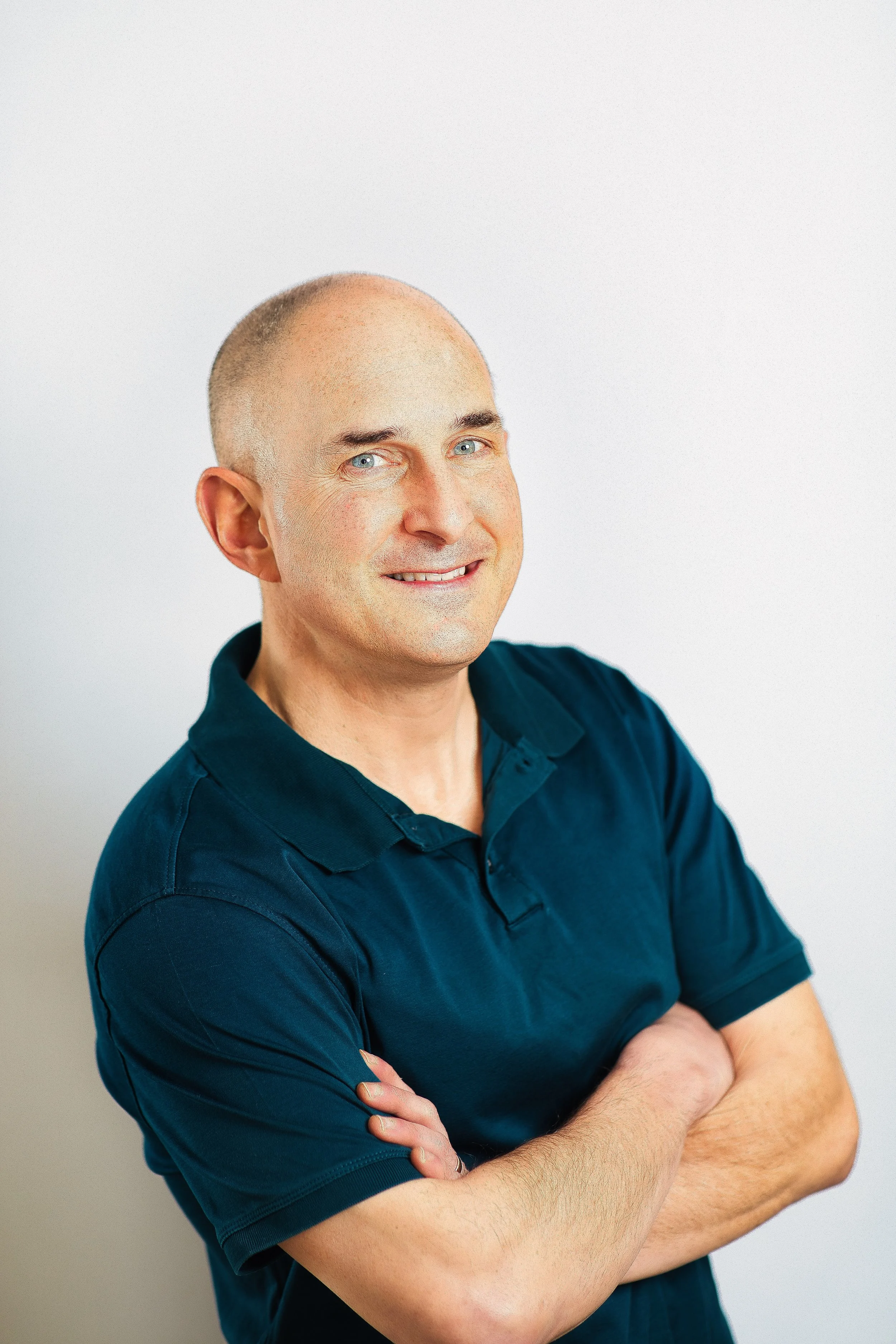 Modern branding headshot of man in green polo with arms crossed, clean background