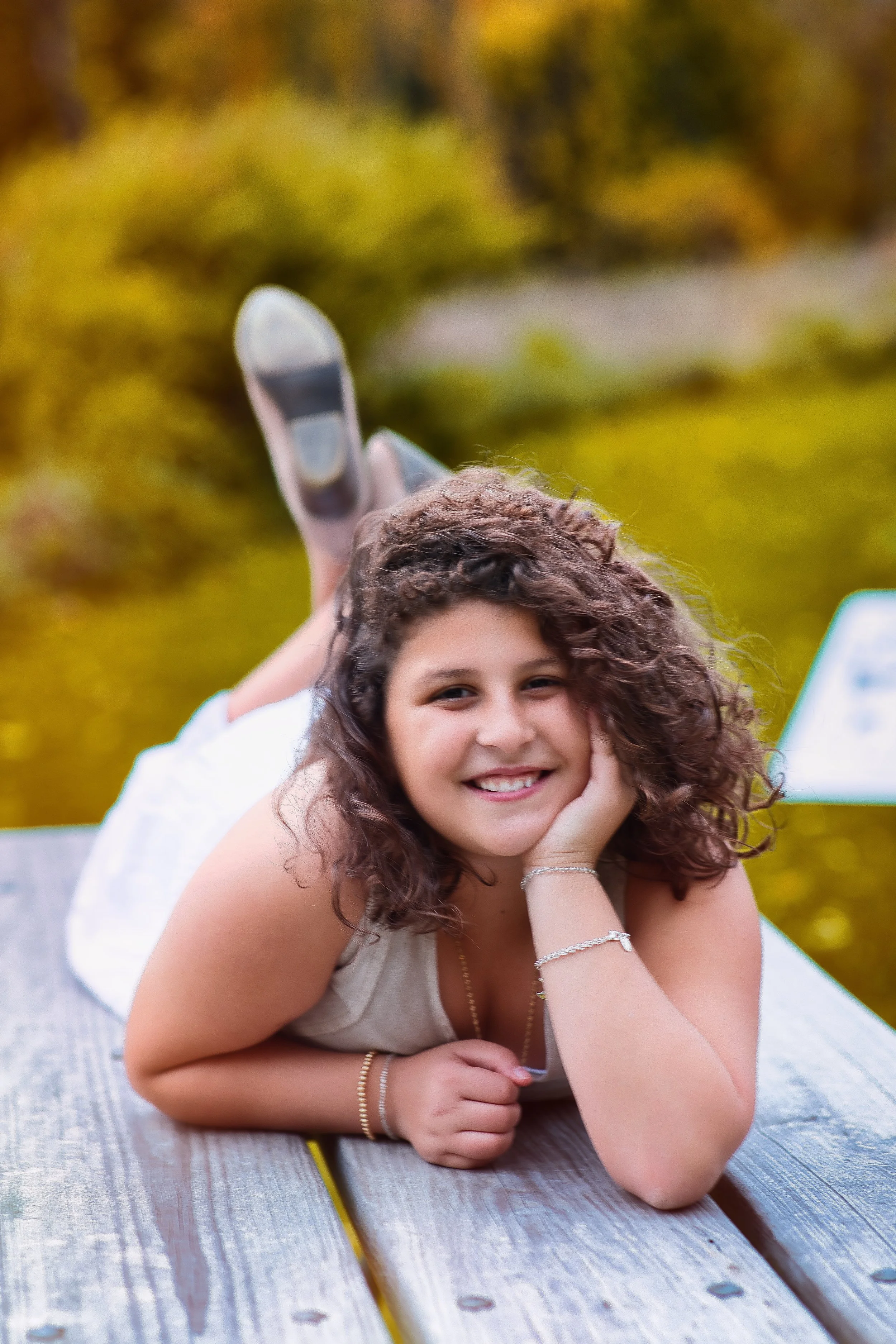 Rochester, NY portrait of a young girl lying on a bench and smiling outdoors with soft fall background