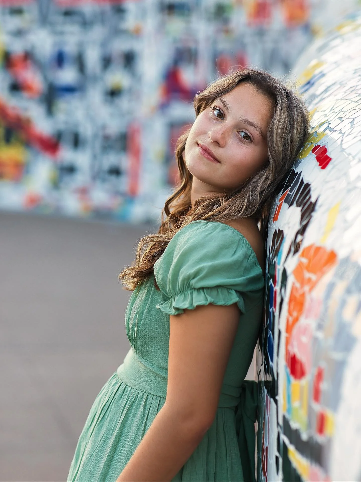 Senior girl in green puff-sleeve top leaning against colorful mosaic mural, urban senior portraits Memorial Art Gallery Rochester NY