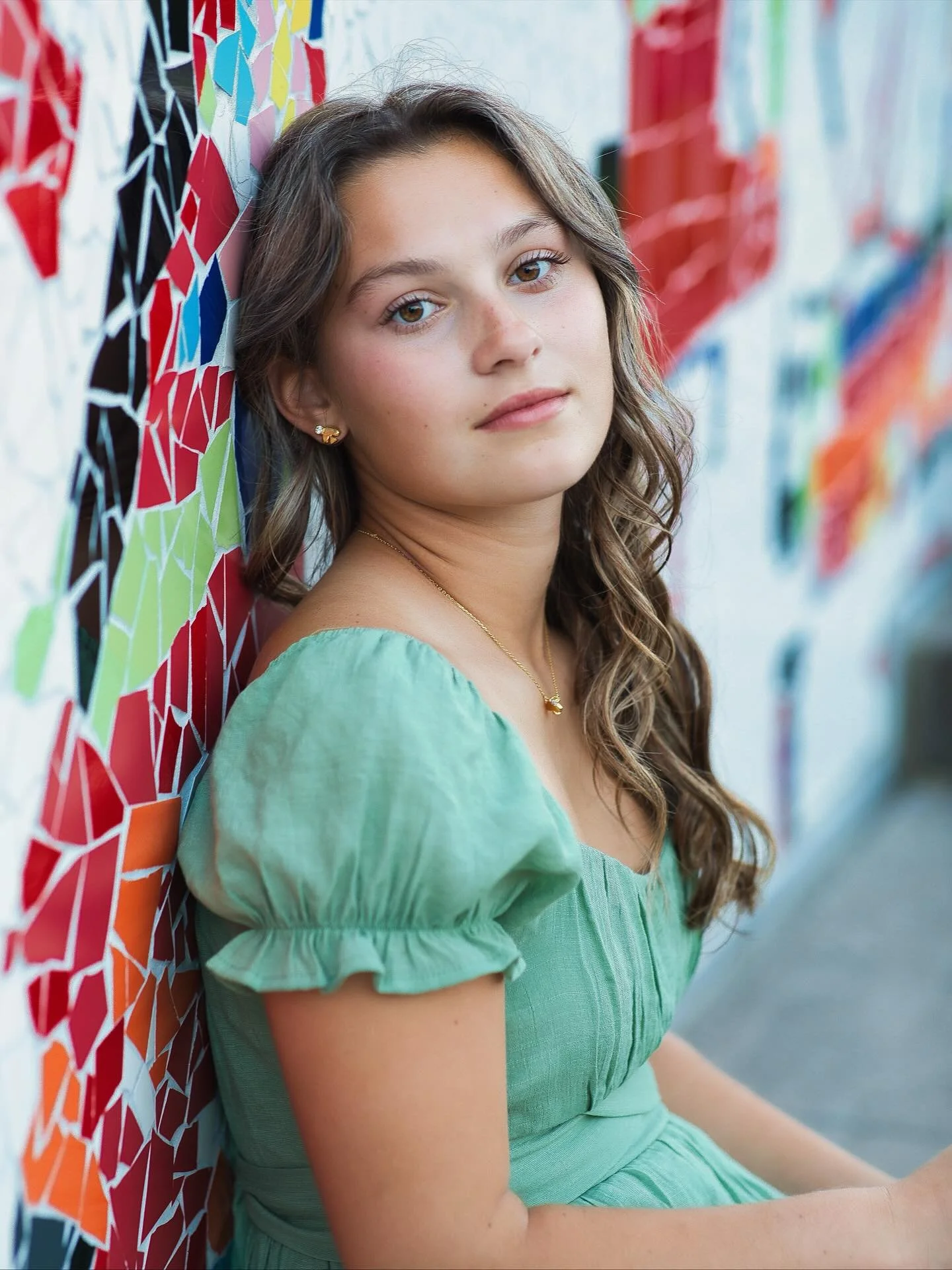 Senior girl in green puff-sleeve top posed against colorful mosaic mural wall, Memorial Art Gallery Rochester NY senior portraits