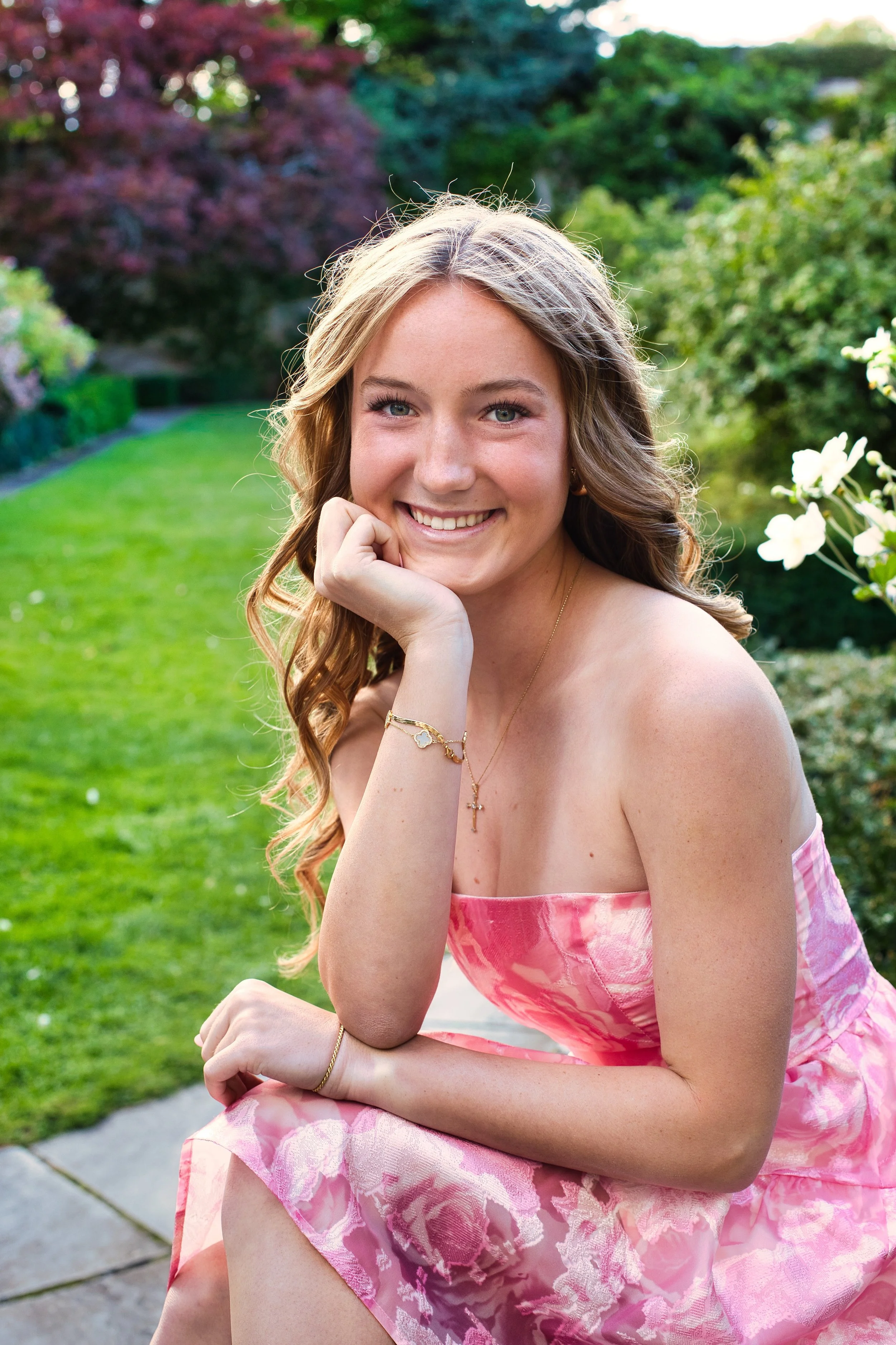 Close-up senior portrait of smiling girl in pink strapless dress in lush garden, George Eastman House Rochester NY senior photography