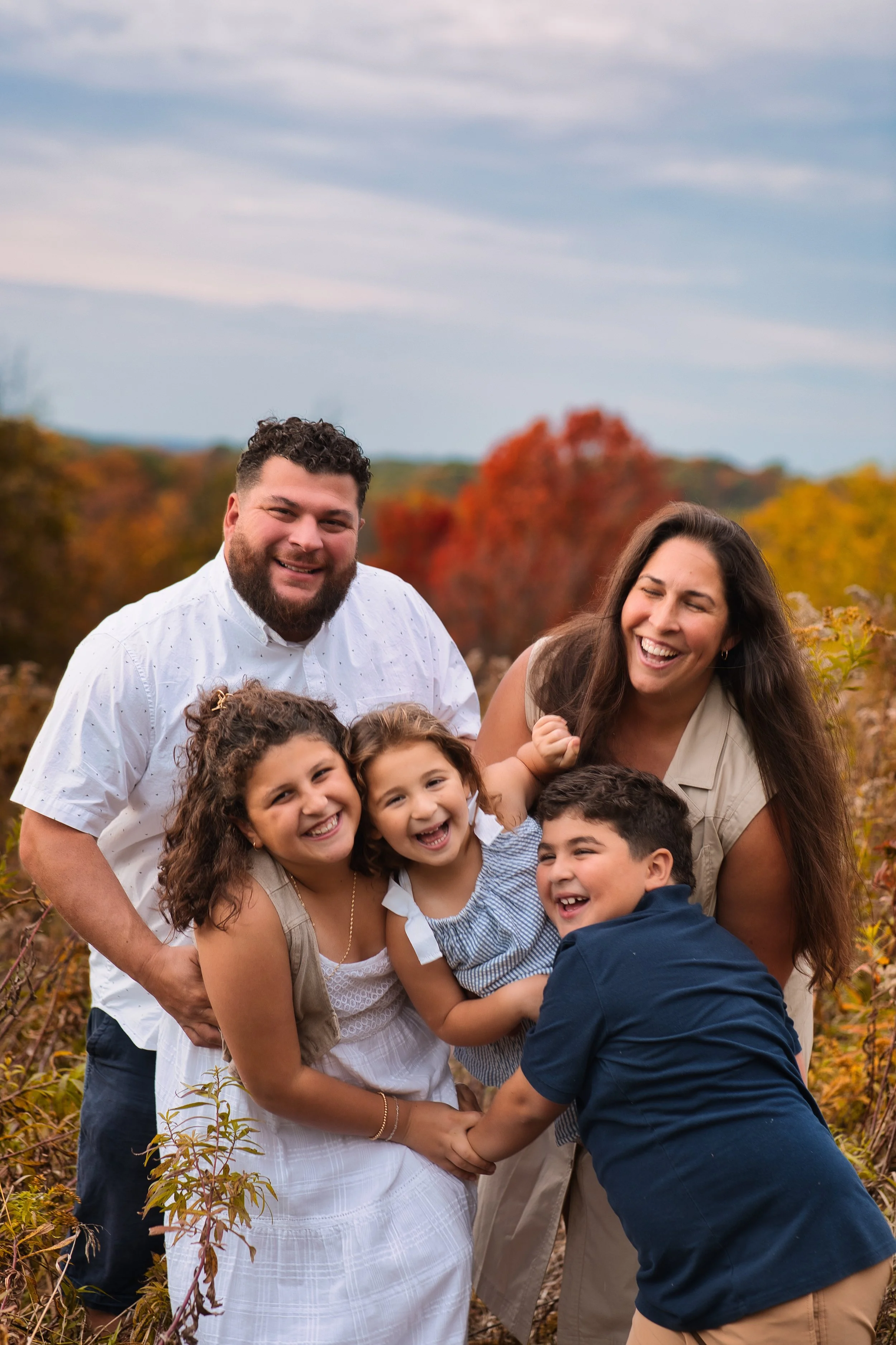 Rochester, NY family portrait of parents and children smiling together with fall foliage background