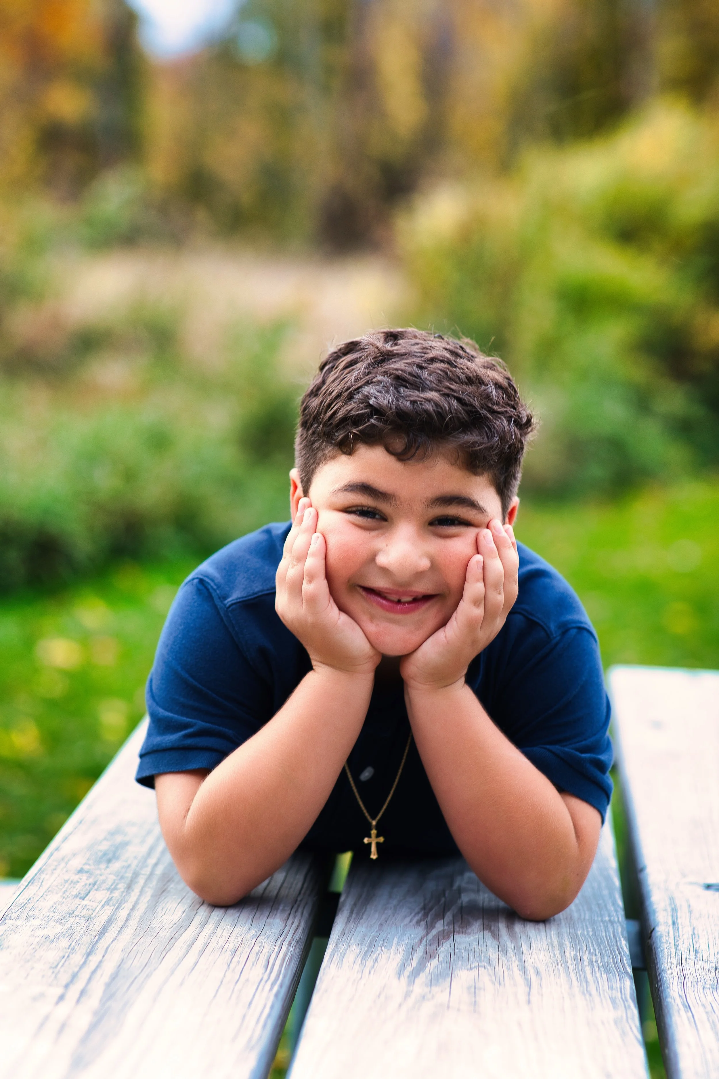 Rochester, NY portrait of a young boy resting his face in his hands and smiling outdoors