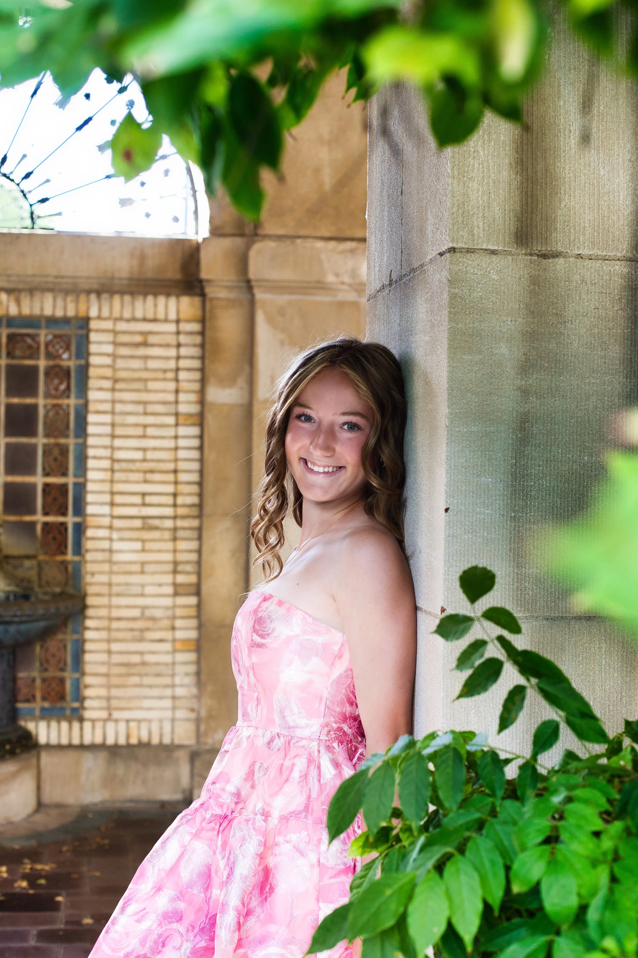 Senior girl in pink semi-formal dress leaning against stone wall pillar surrounded by ivy, George Eastman House Rochester NY senior portraits