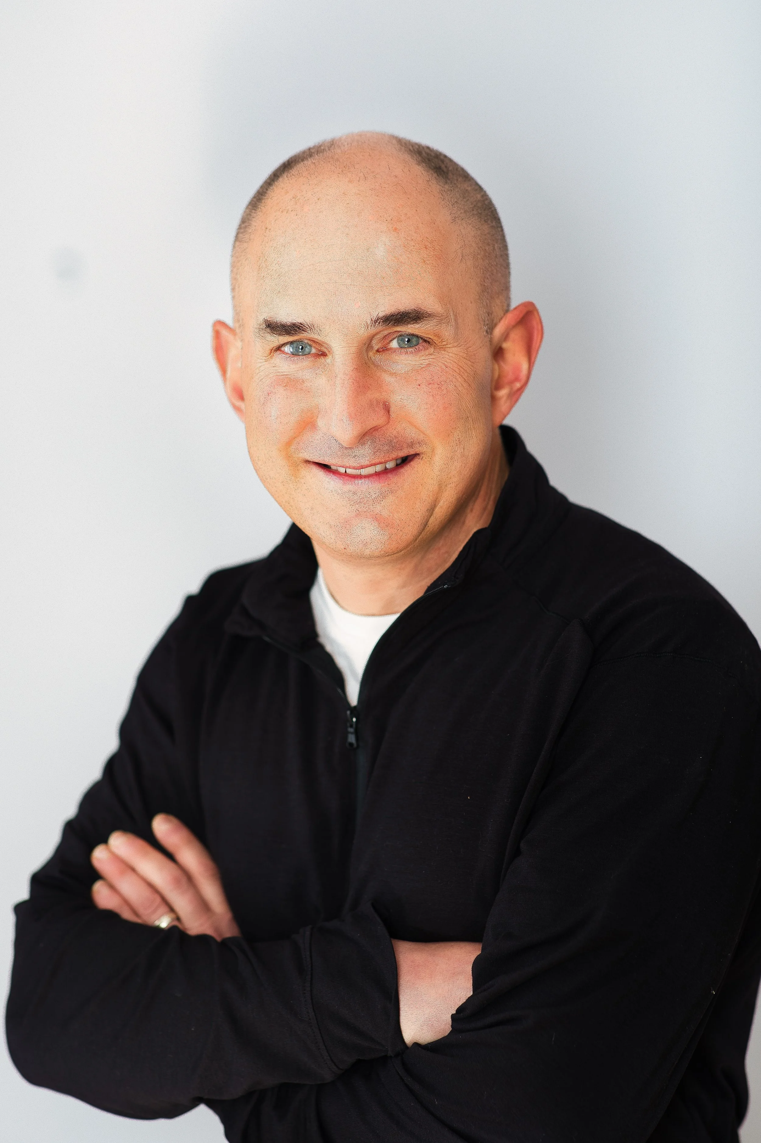 Casual professional headshot of man in black quarter-zip, smiling against neutral background