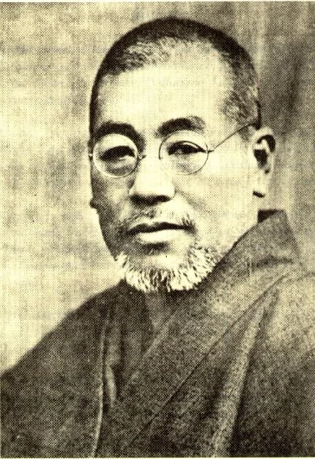 Black and white portrait of an Asian man with short hair, round glasses, and a beard, wearing traditional clothing.