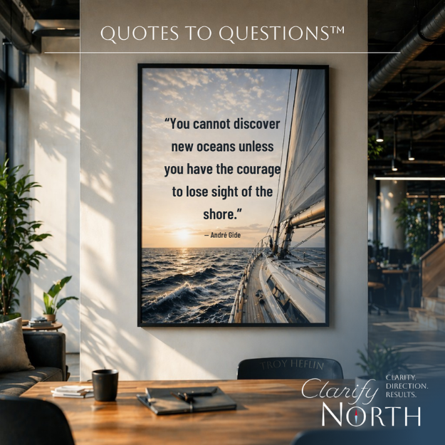 A large framed quote about courage and discovering new oceans hangs on a white wall in a modern office space, with a photo of a sailboat on the ocean at sunset. The office has a wooden table with a cup, notebook, and pen, and a black chair. The top of the image reads "Quotes to Questions™" and the bottom right corner contains the logo and tagline for "Clarity North."