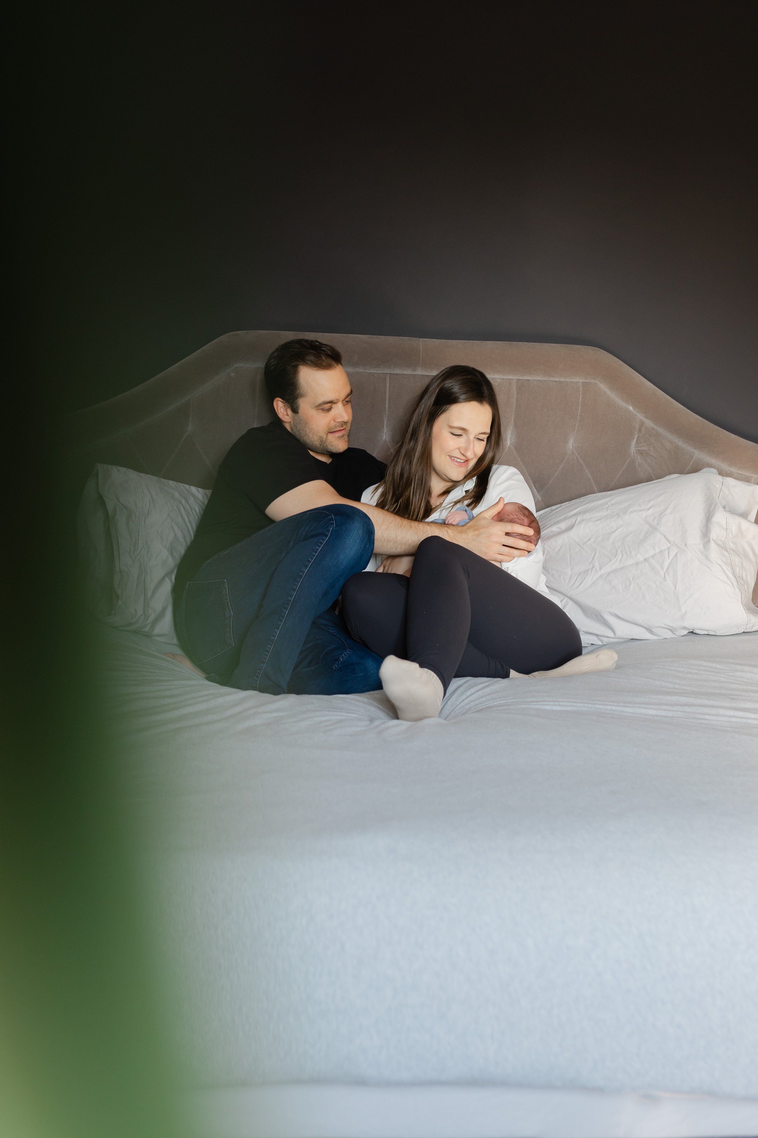 A couple sitting on a bed, holding a baby, looking content and happy.