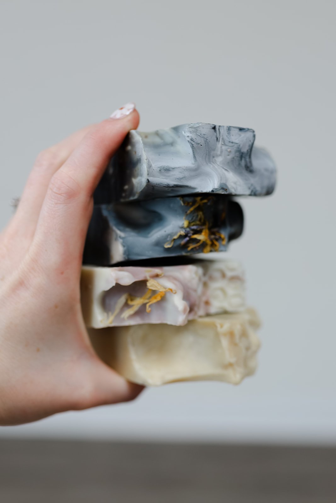 Hand holding stack of four artisan soaps of different colors and textures
