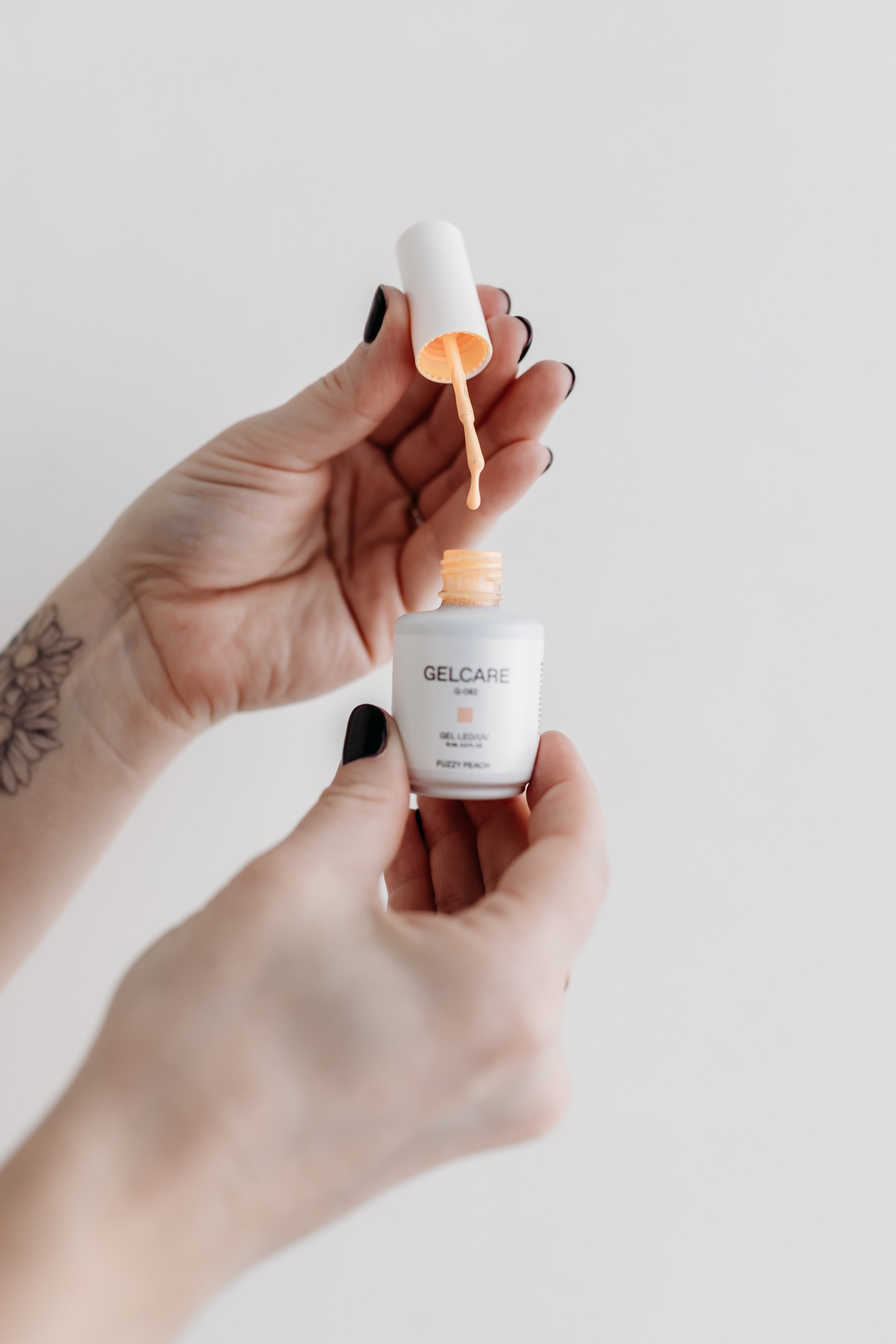 Hands holding a small bottle of Gelcare gel polish with an open cap and brush.