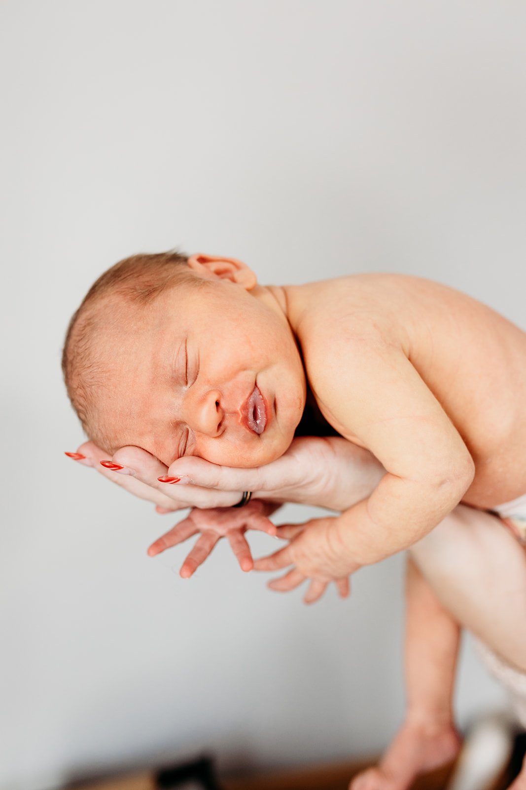 Newborn baby sleeping on a person's hands with a neutral background.