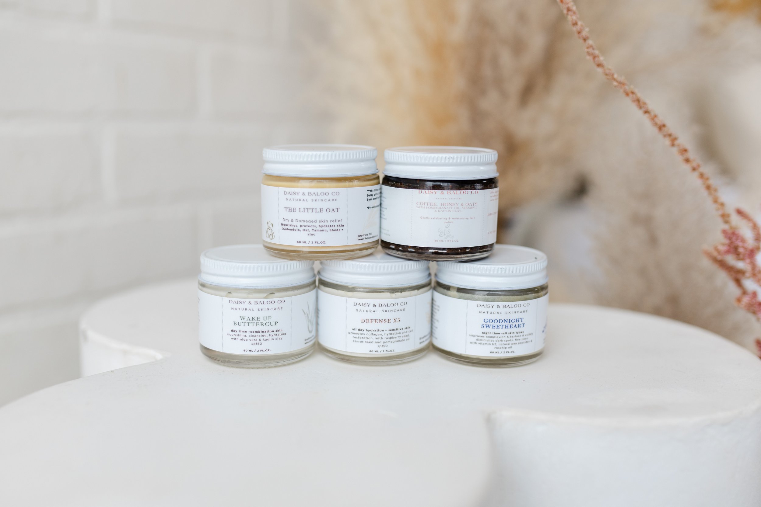 Five jars of Daisy & Baloo Co natural skincare products displayed on a round white surface with a neutral background.