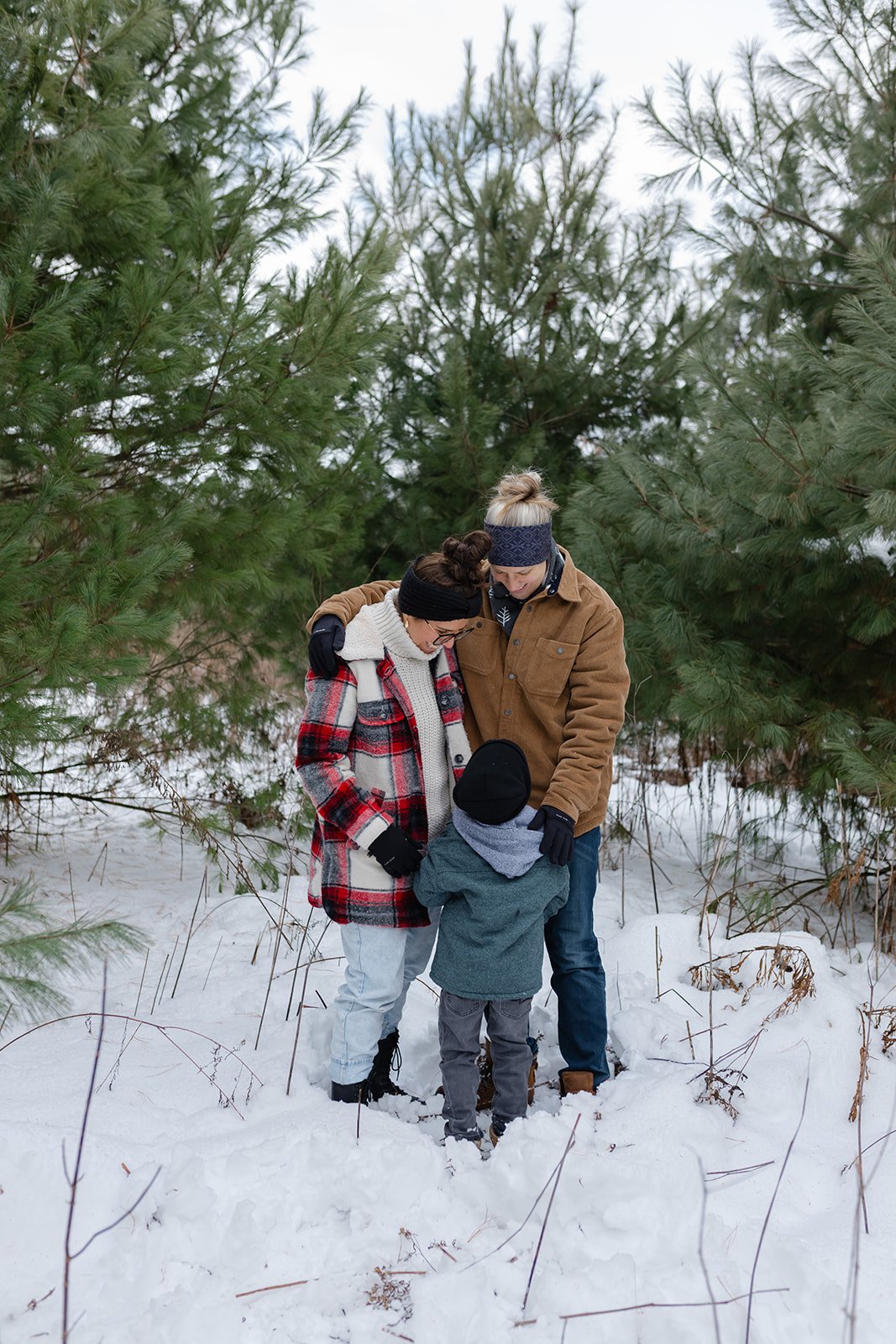 Family standing in snow with pine trees, wearing winter clothing.