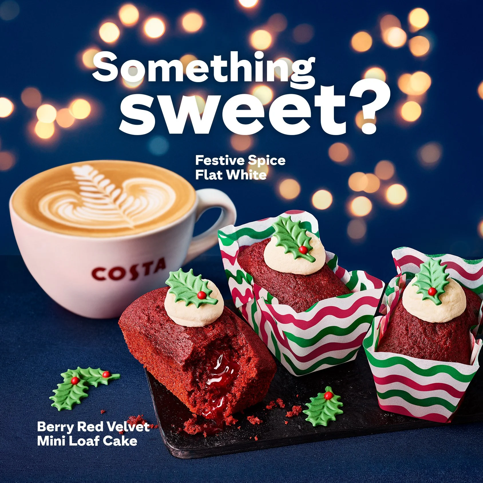 Cup of Costa coffee labeled 'Festive Spice Flat White' next to three berry red velvet mini loaf cakes with holiday-themed decorations, on a blue background with bokeh lights. Text reads 'Something sweet?'.