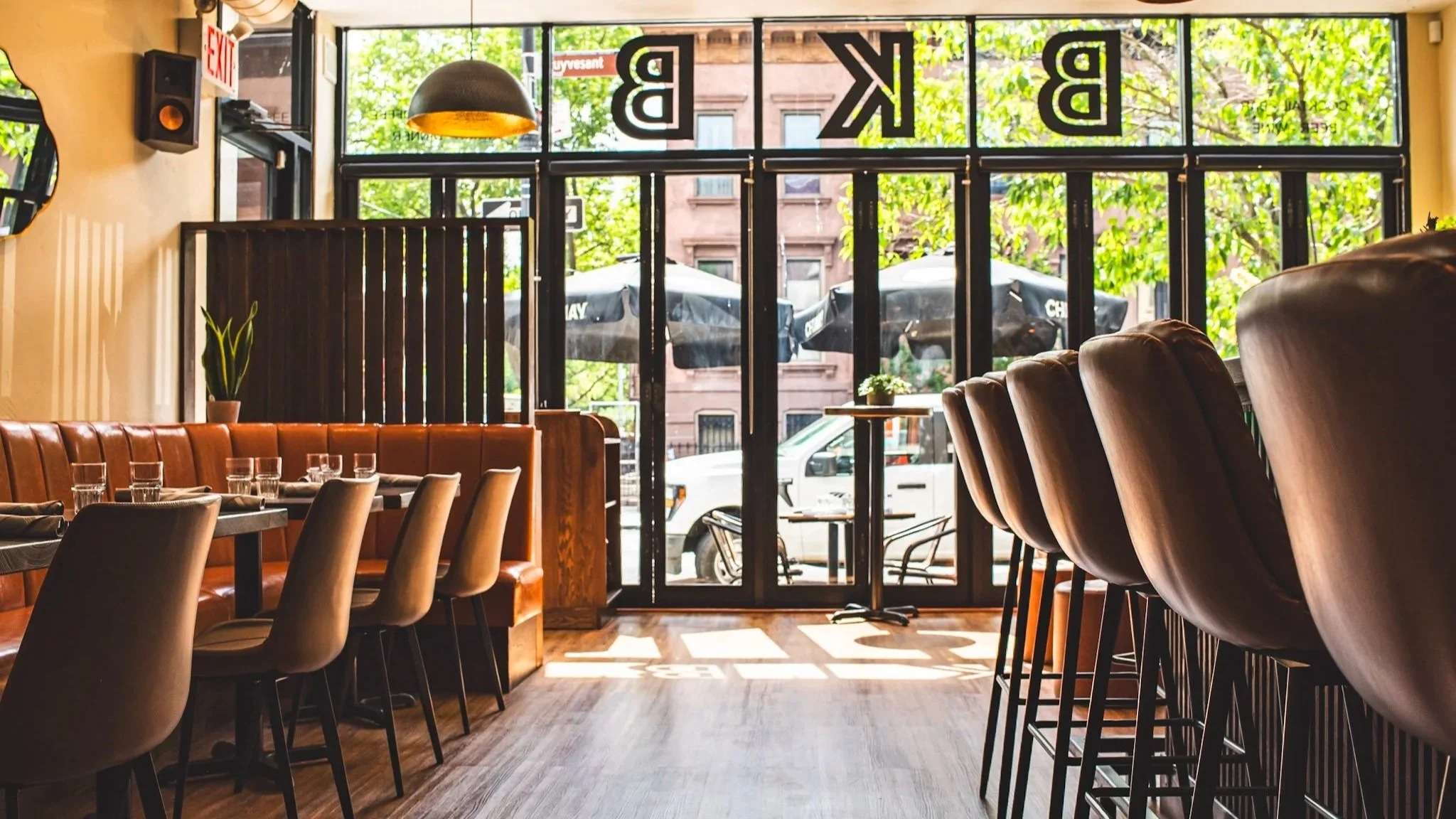 Interior of BKB Brooklyn Brasserie with bright natural light streaming through large glass windows and doors.