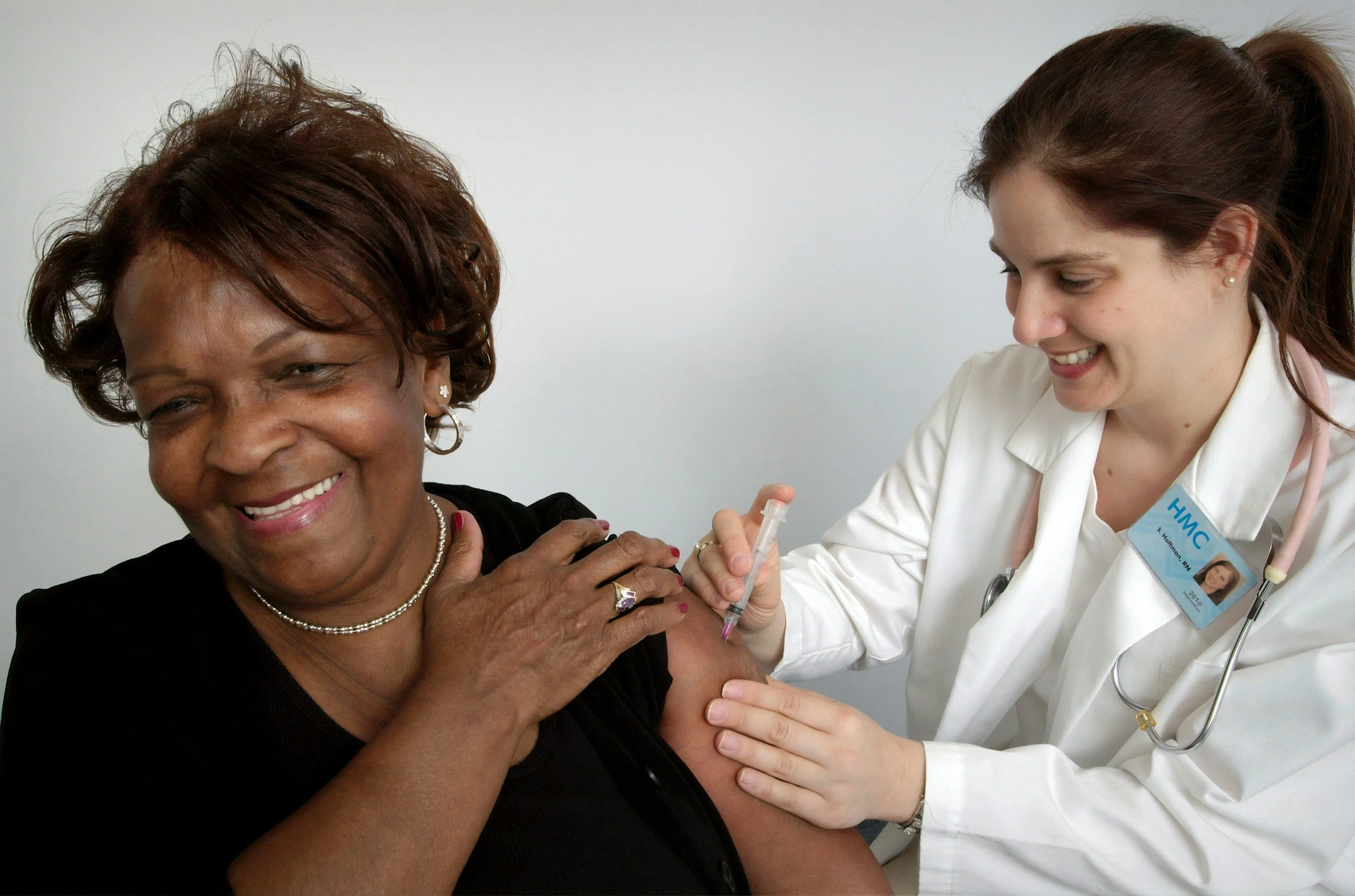 A healthcare professional administering a vaccine to a smiling woman.