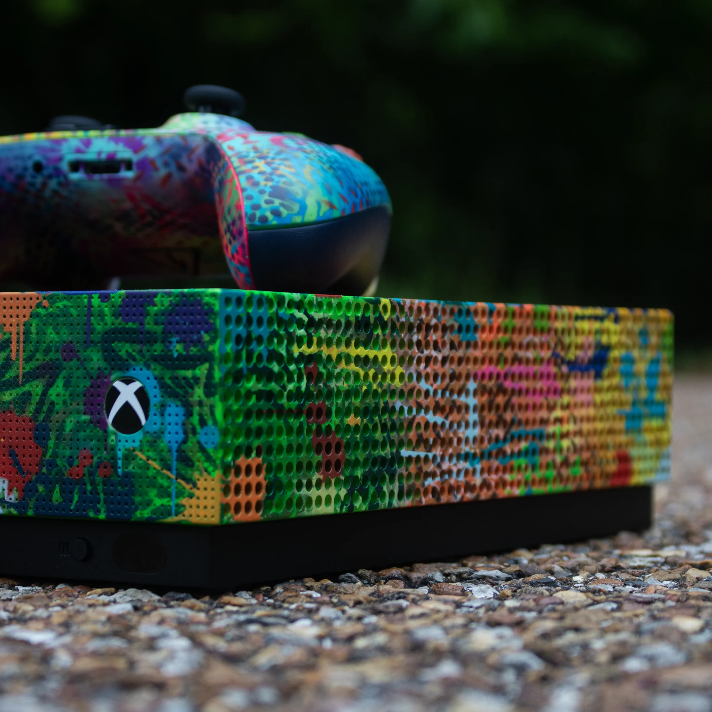 Close-up of a colorful gaming controller resting on a gravel surface with a dark blurred background.